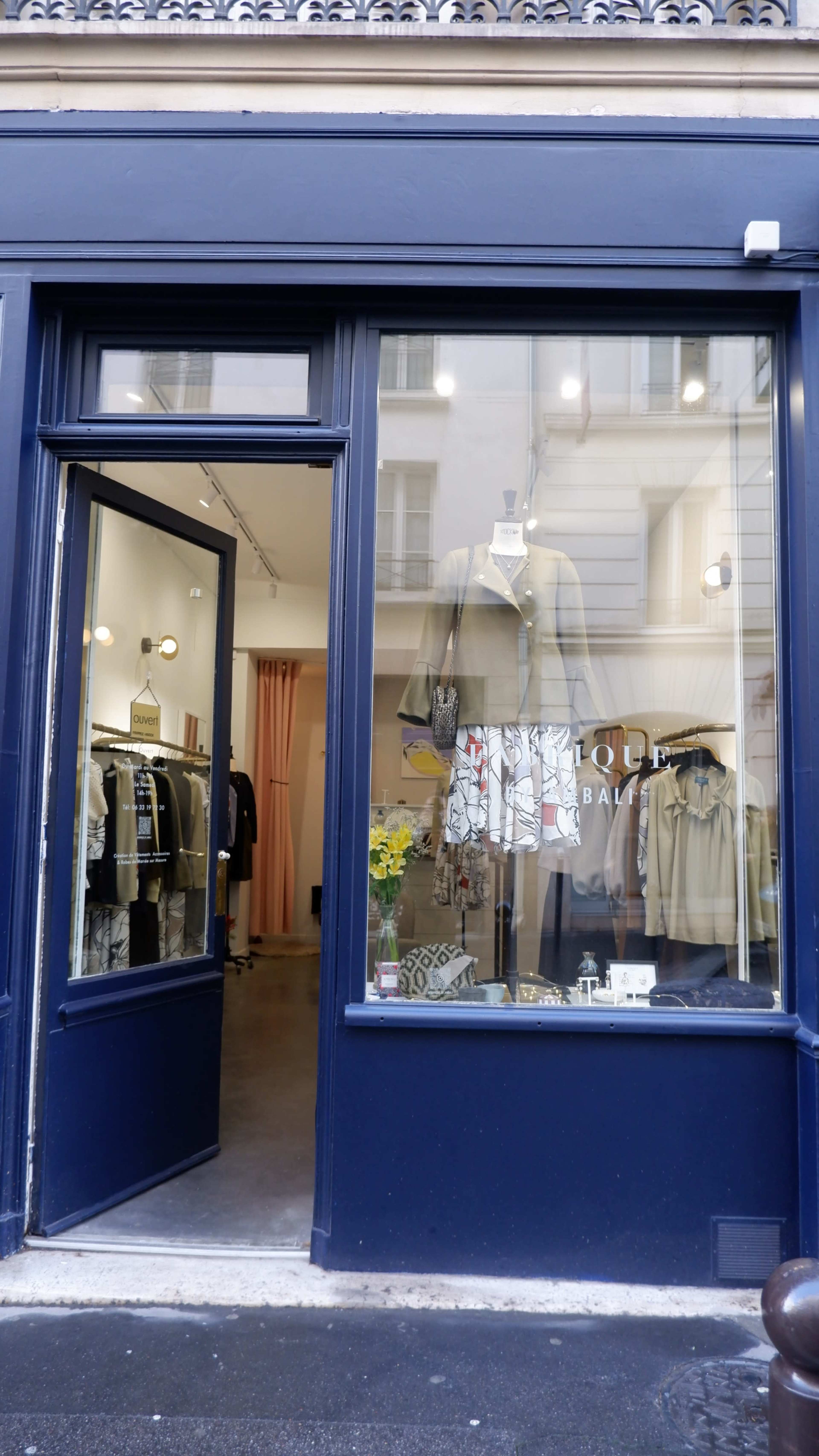 A storefront with a navy blue facade displaying clothing and accessories inside, including a floral arrangement in the window.