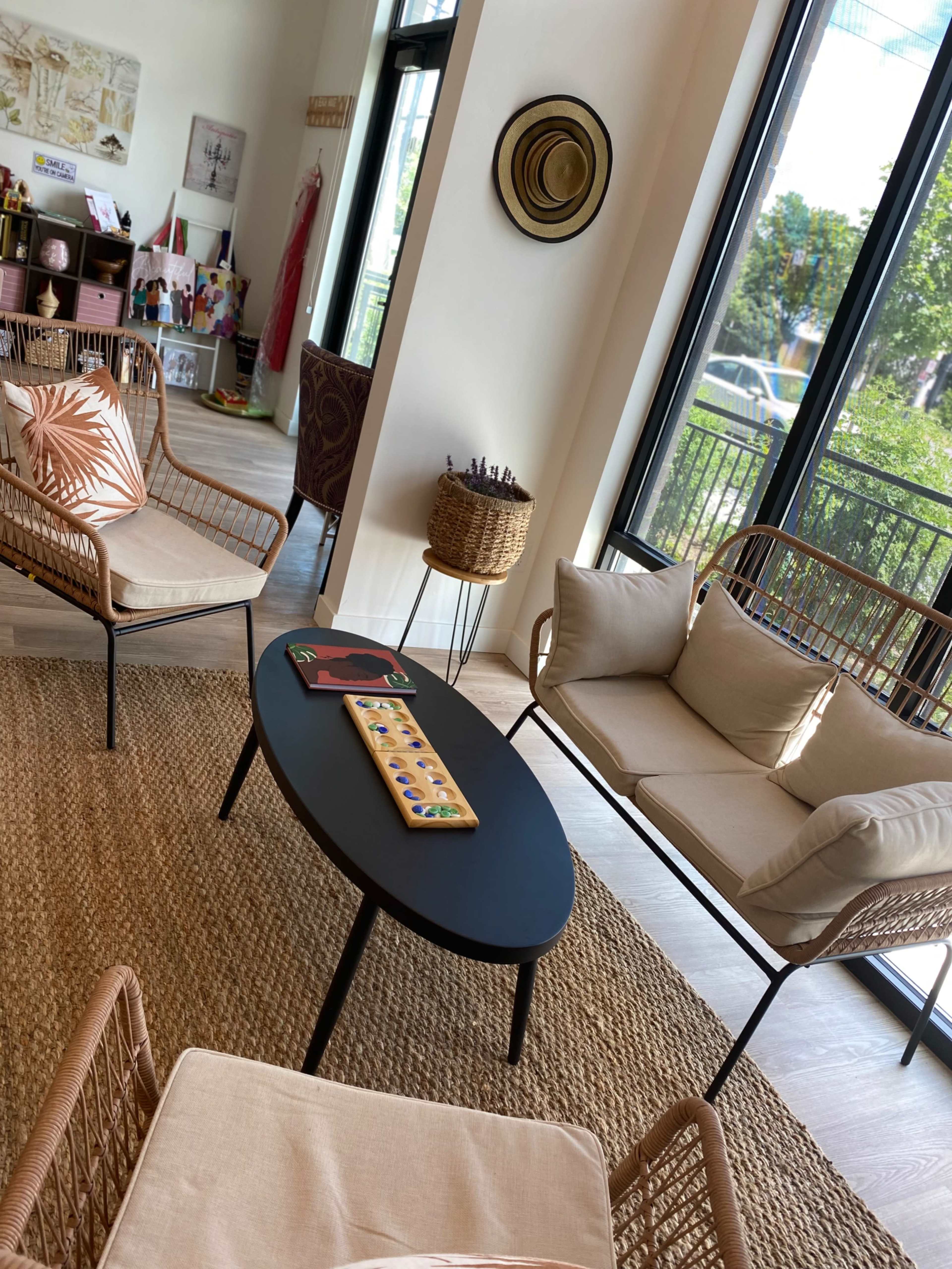 A modern living space with two woven chairs, a black oval coffee table, and large windows that let in natural light.