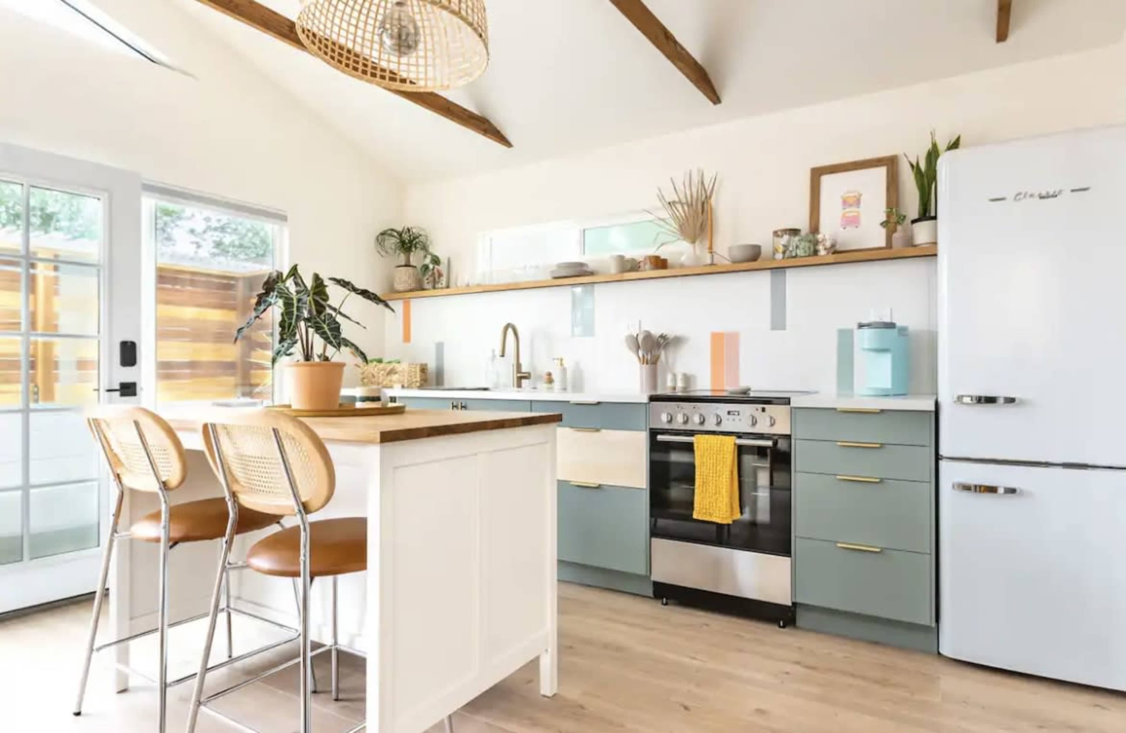 A modern kitchen features a central island, stainless steel appliances, and light wood accents with green cabinetry.