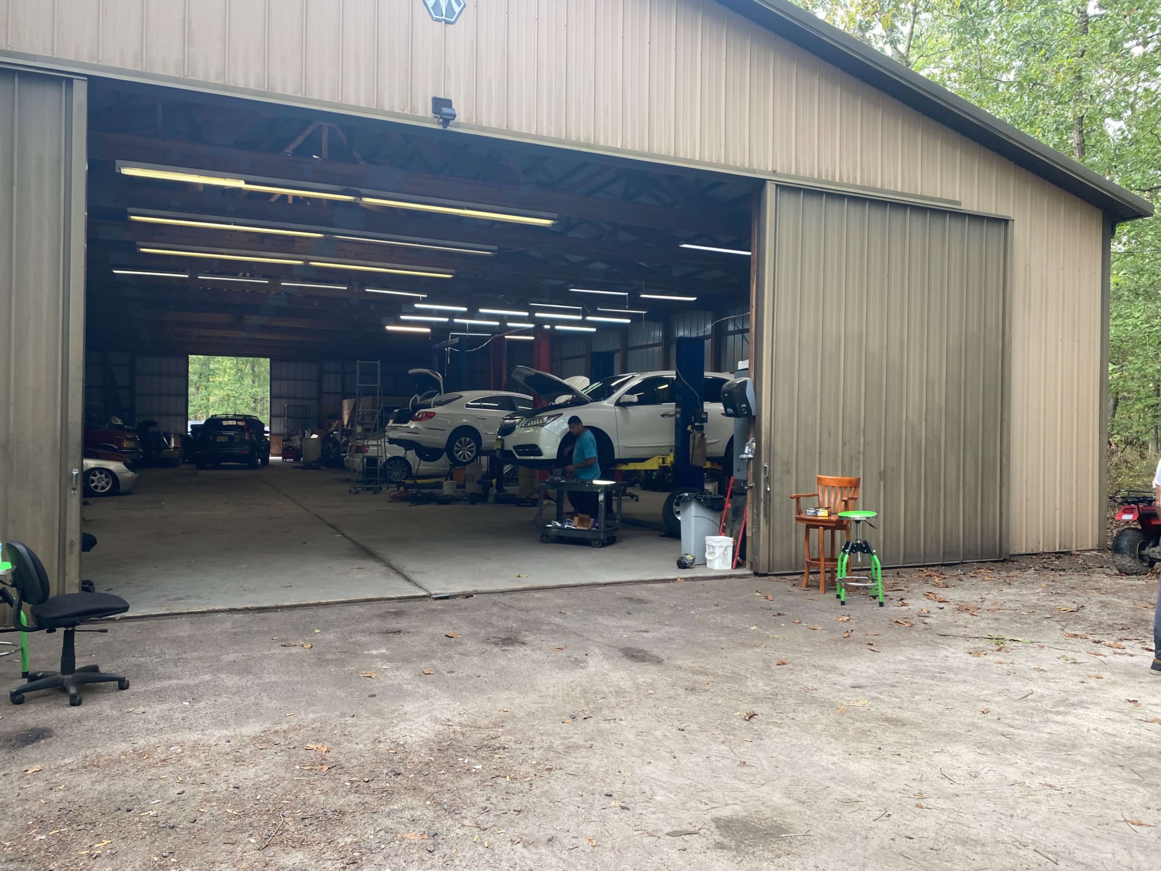 A vehicle repair shop with several cars on lifts, tools, and equipment inside a large garage.