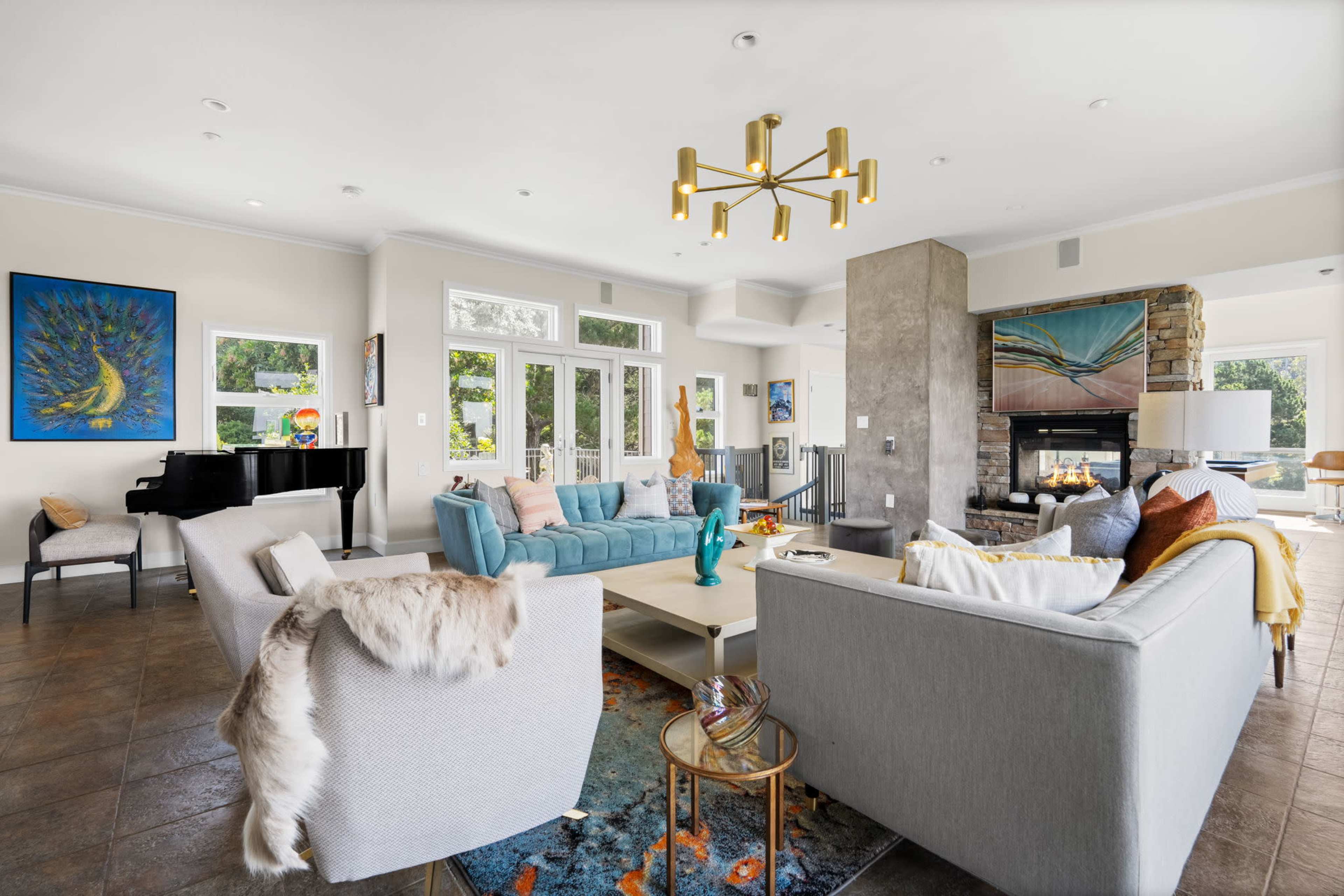 A spacious, well-lit living room features a mix of comfortable seating arrangements, a fireplace, and large windows.