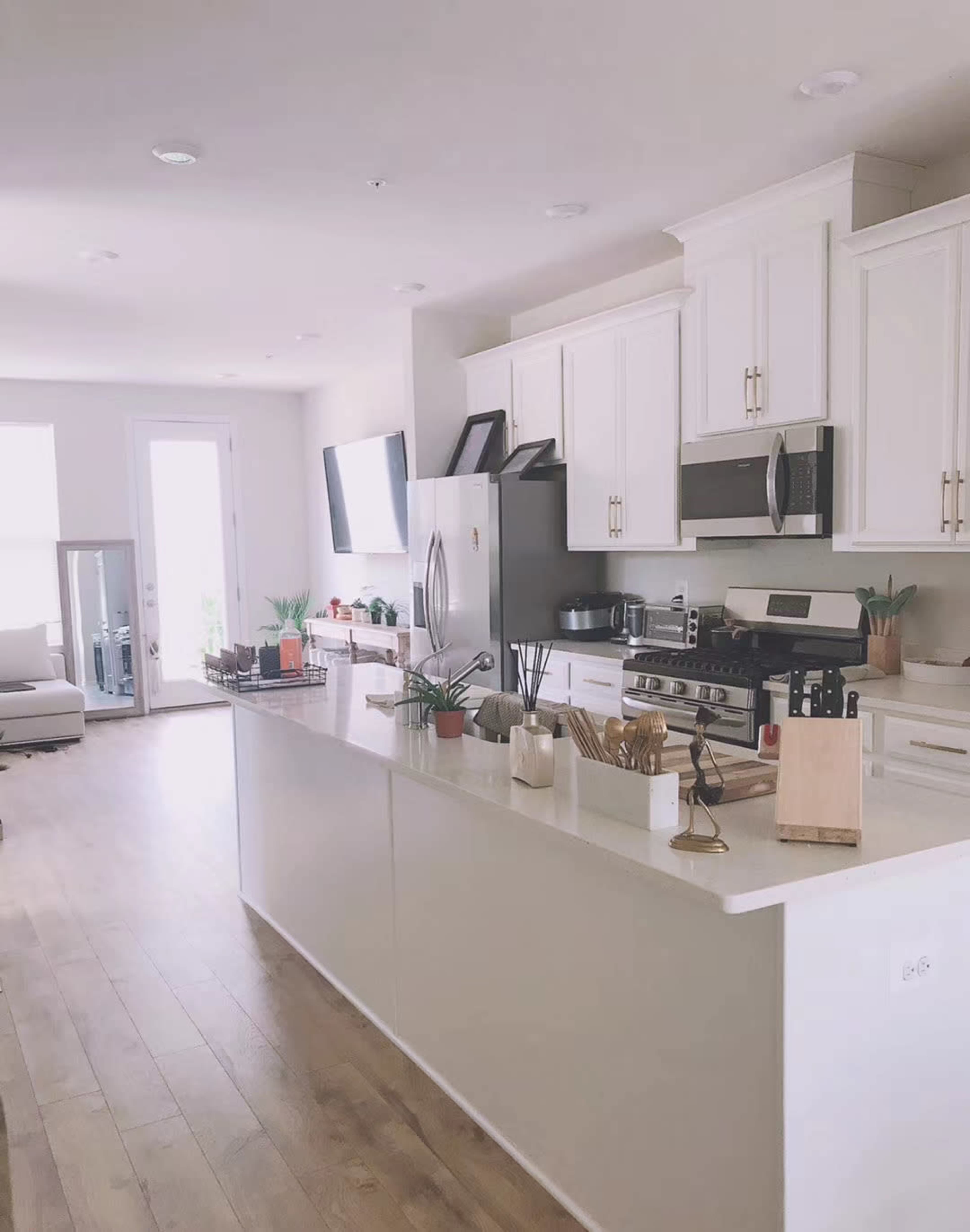 The image shows a modern kitchen with white cabinets, stainless steel appliances, and a large island featuring minimal decor and cooking utensils.