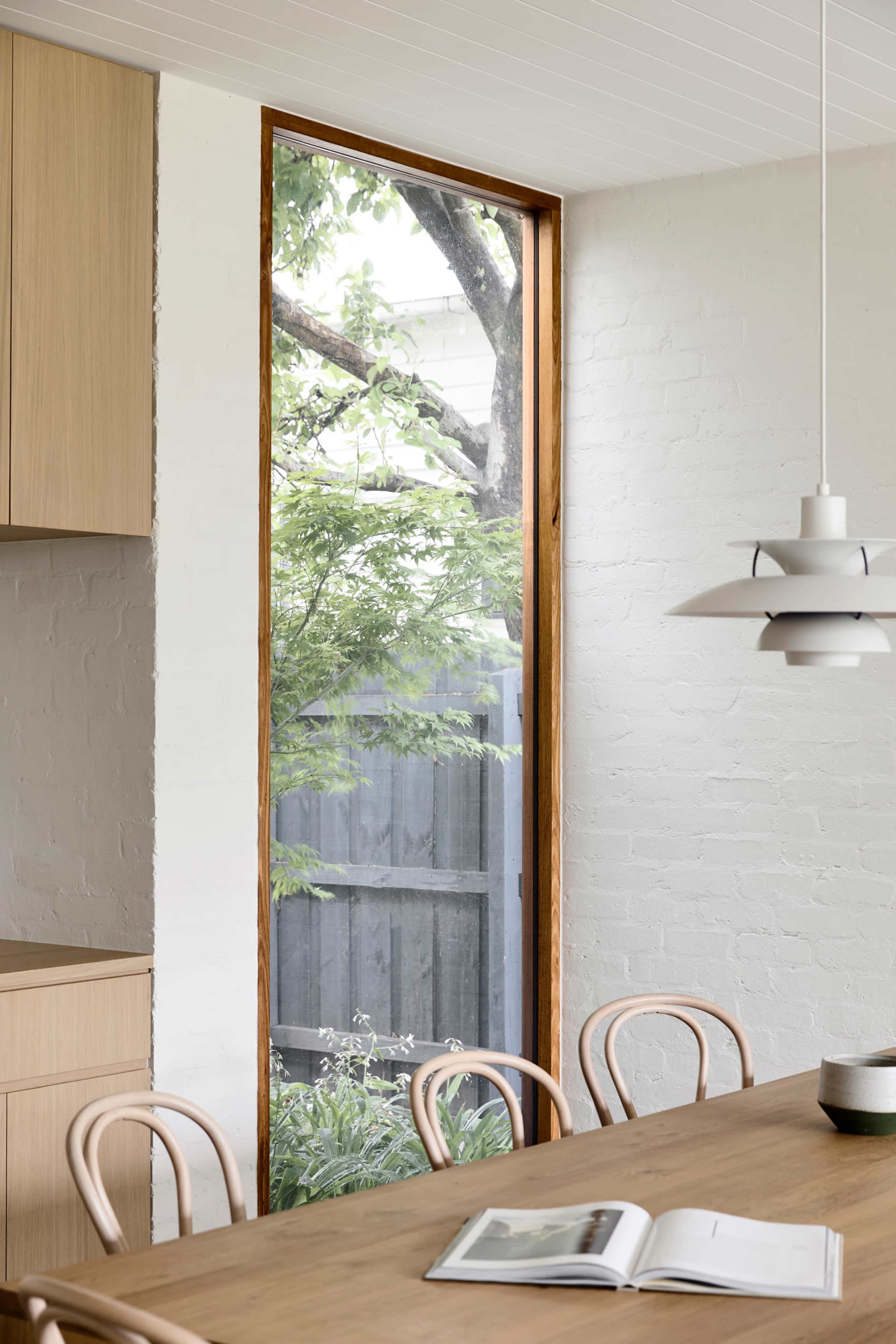 A wooden-framed window reveals a view of greenery and a wooden fence in an interior dining space.