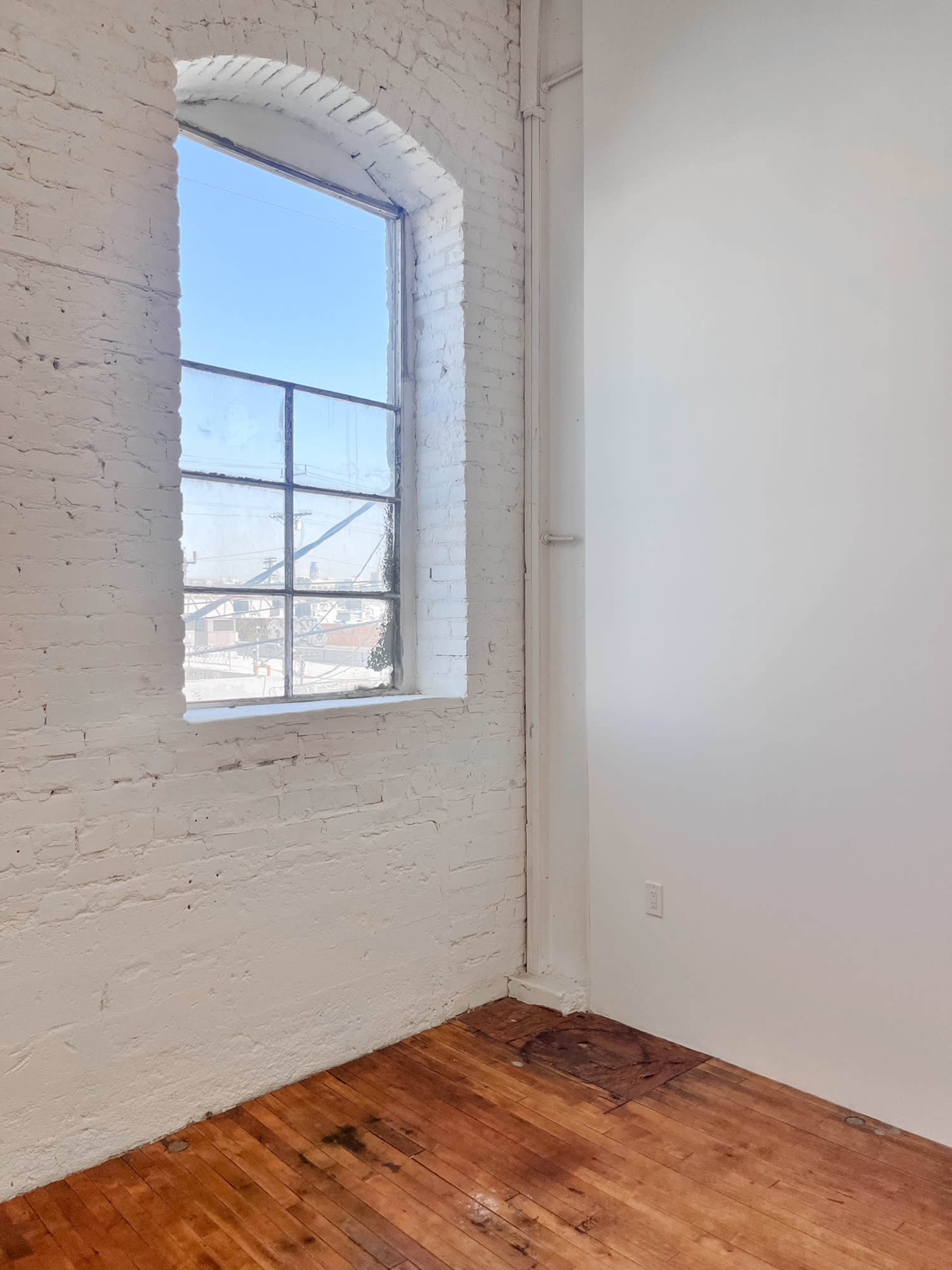 A bright, empty room with a large arched window and exposed brick walls.