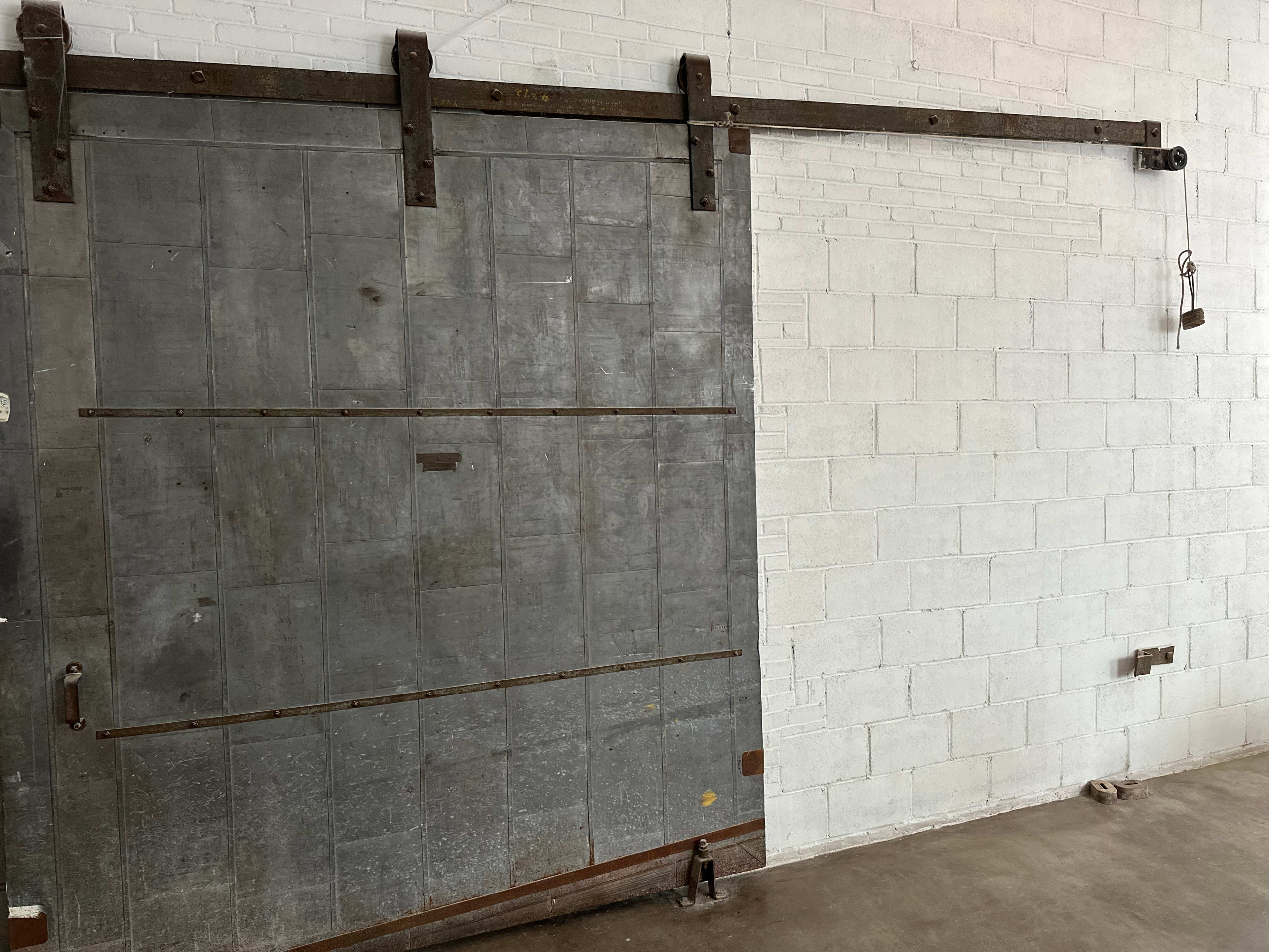 A large metal sliding door is mounted on a wall, featuring a rustic design with visible hinges and a sliding track.
