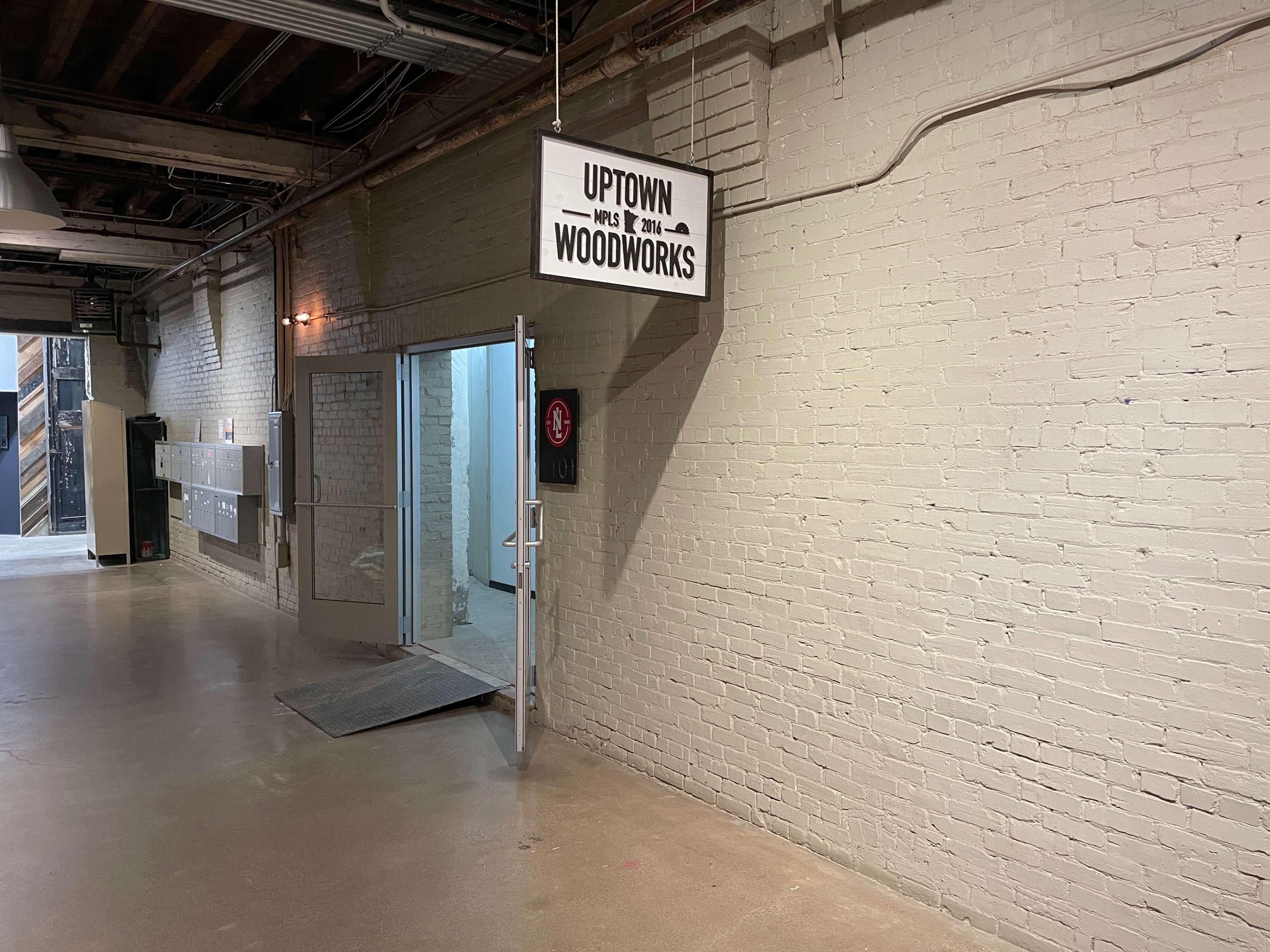 The image shows a hallway with a sign that reads "Uptown Woodworks" above an open door leading to a workshop area.