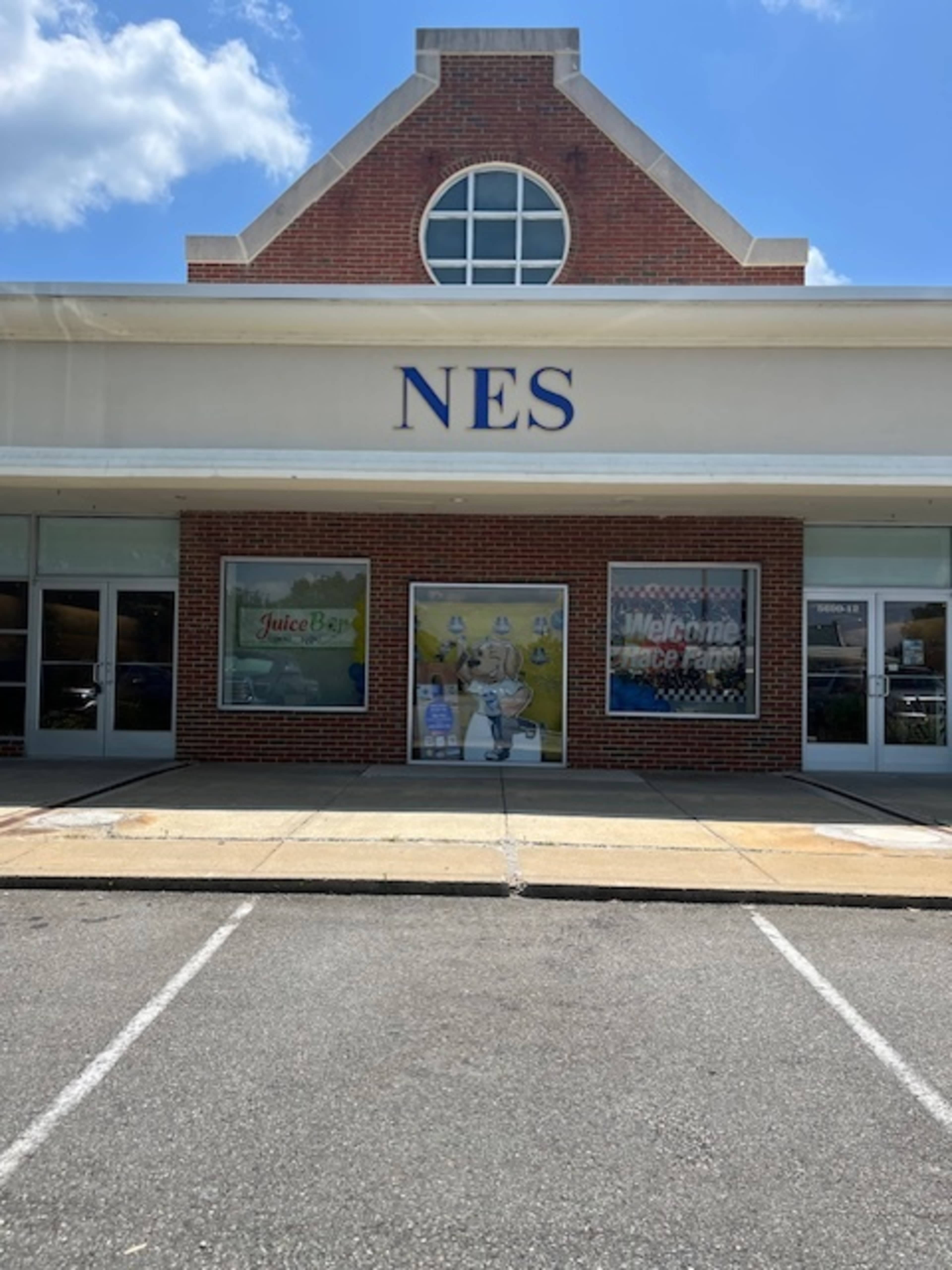 The image shows a building with a sign reading "NES" above its entrance, featuring large windows displaying advertisements and a parking area in front.