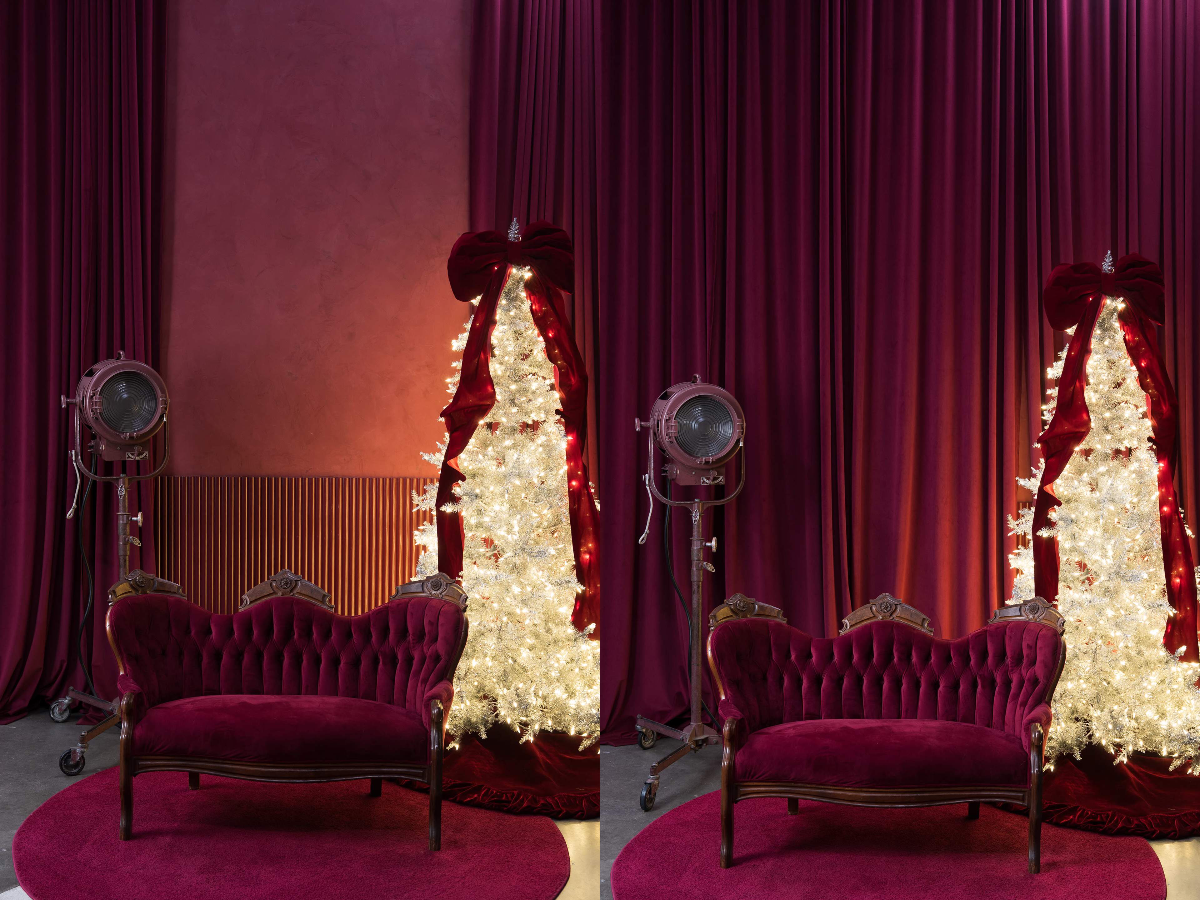 A vintage burgundy couch is positioned in front of a white Christmas tree adorned with red bows, set against a backdrop of rich, burgundy drapes.