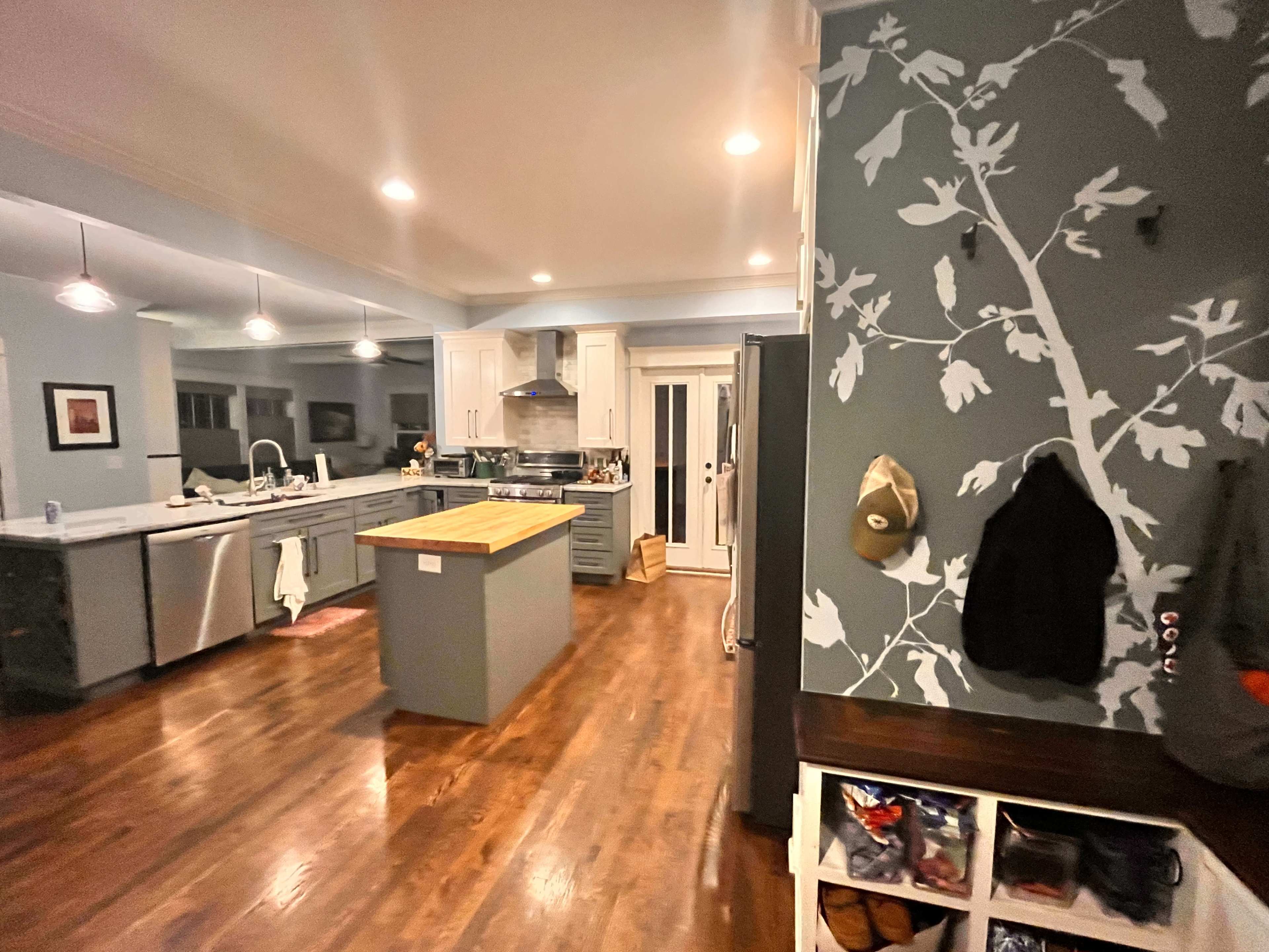 A spacious kitchen with wooden floors, a central island, and modern appliances, featuring an adjacent entryway with a wall of hooks and shoe storage.