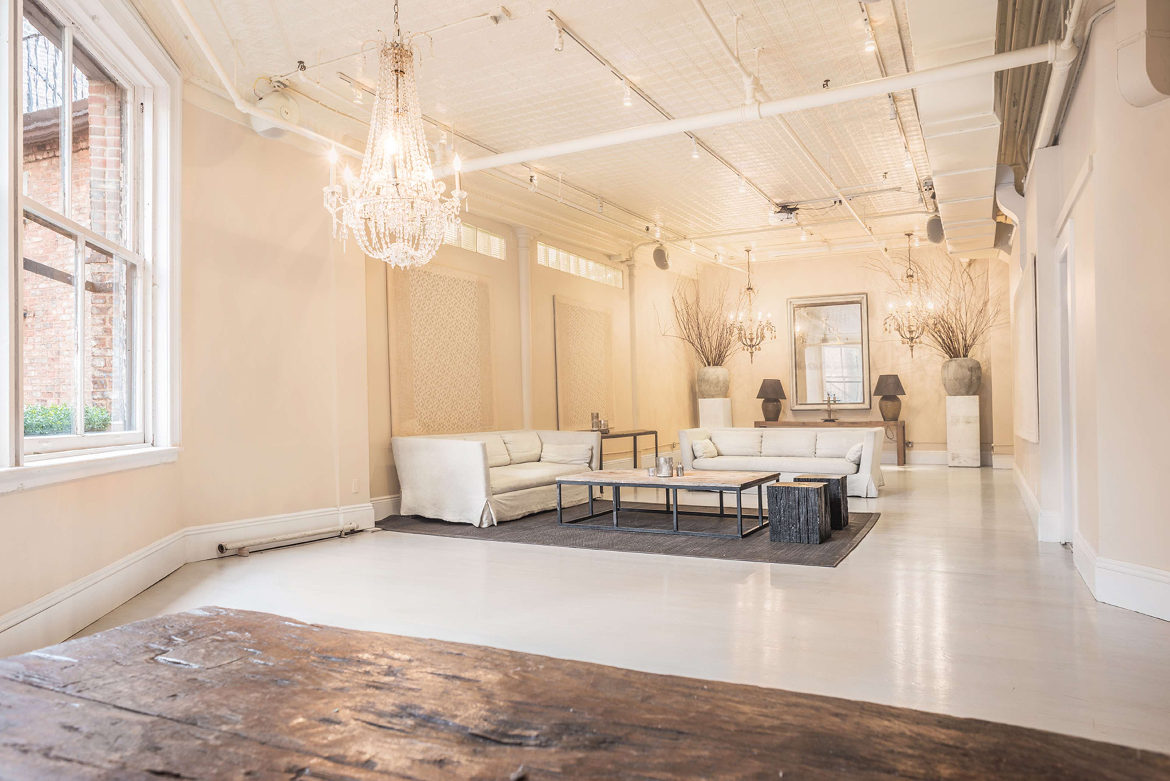 A spacious interior with light-colored walls, a central seating area featuring a white sofa set, a dark area rug, and elegant lighting fixtures.