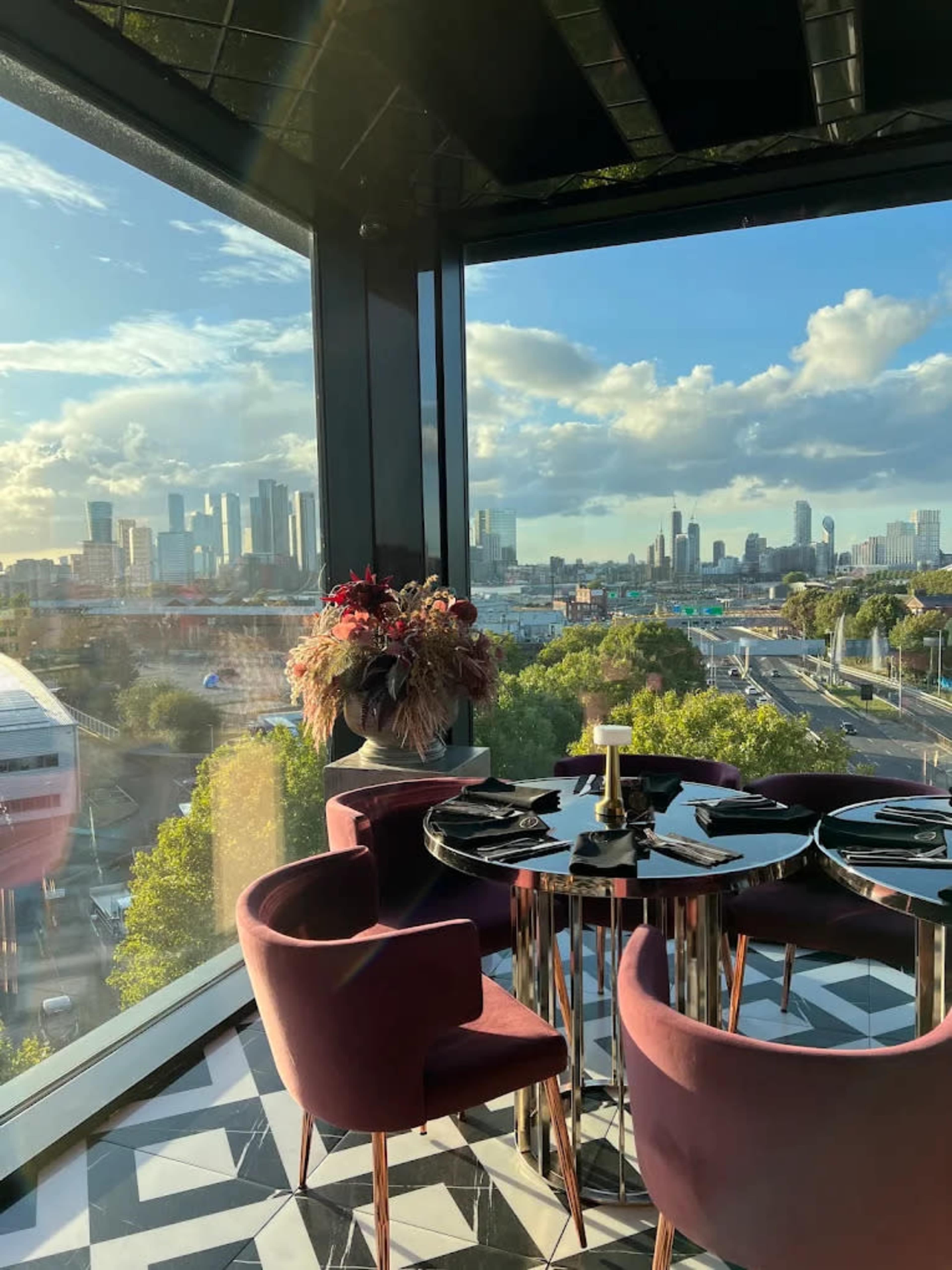 A modern dining area features a round black table set for four, surrounded by plush purple chairs and large windows showcasing a skyline view.