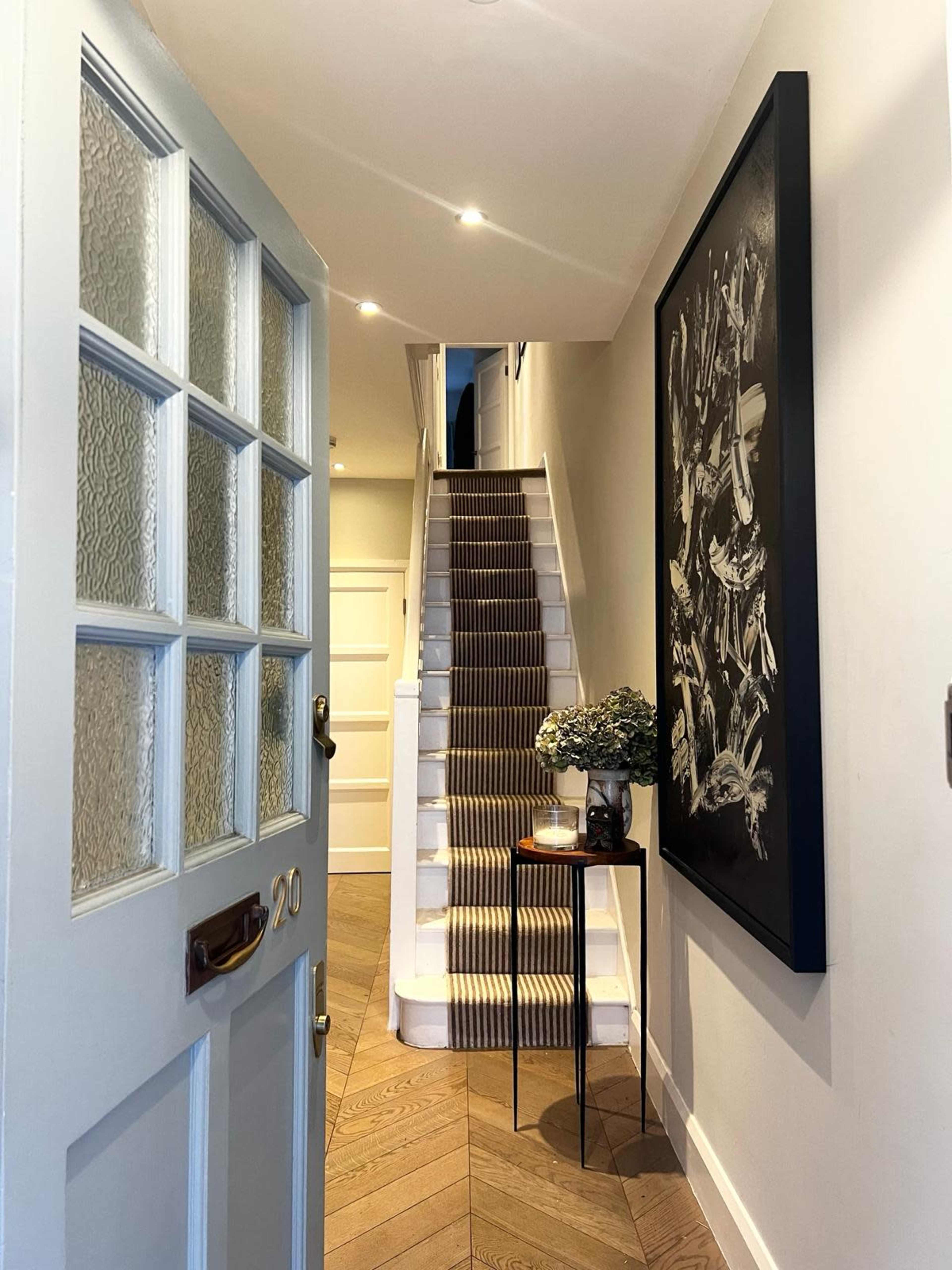 A doorway opens to a hallway with a staircase leading up and a piece of artwork on the adjacent wall.