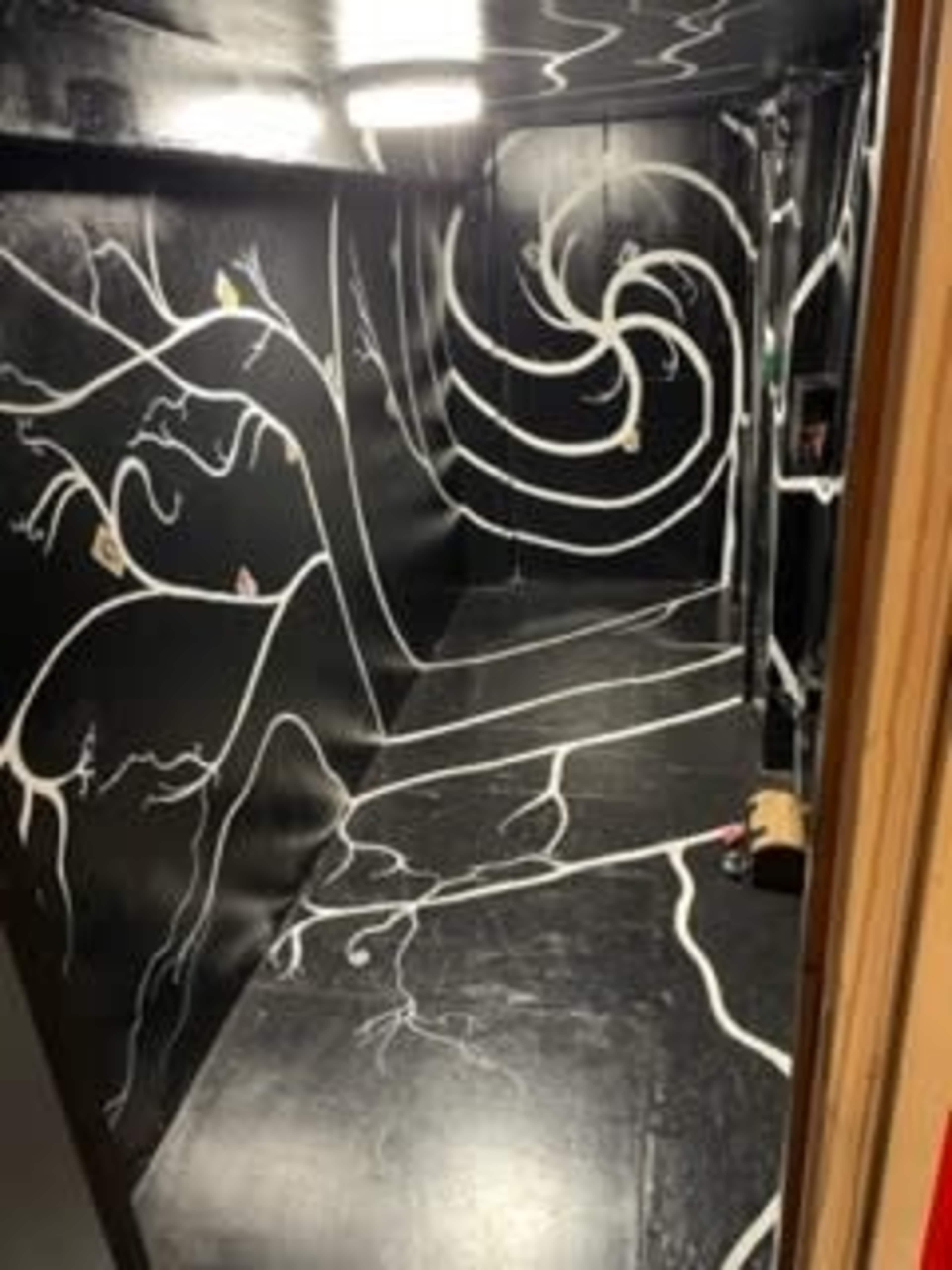 A dimly lit room with black walls and floor, featuring swirling white lines and abstract designs.