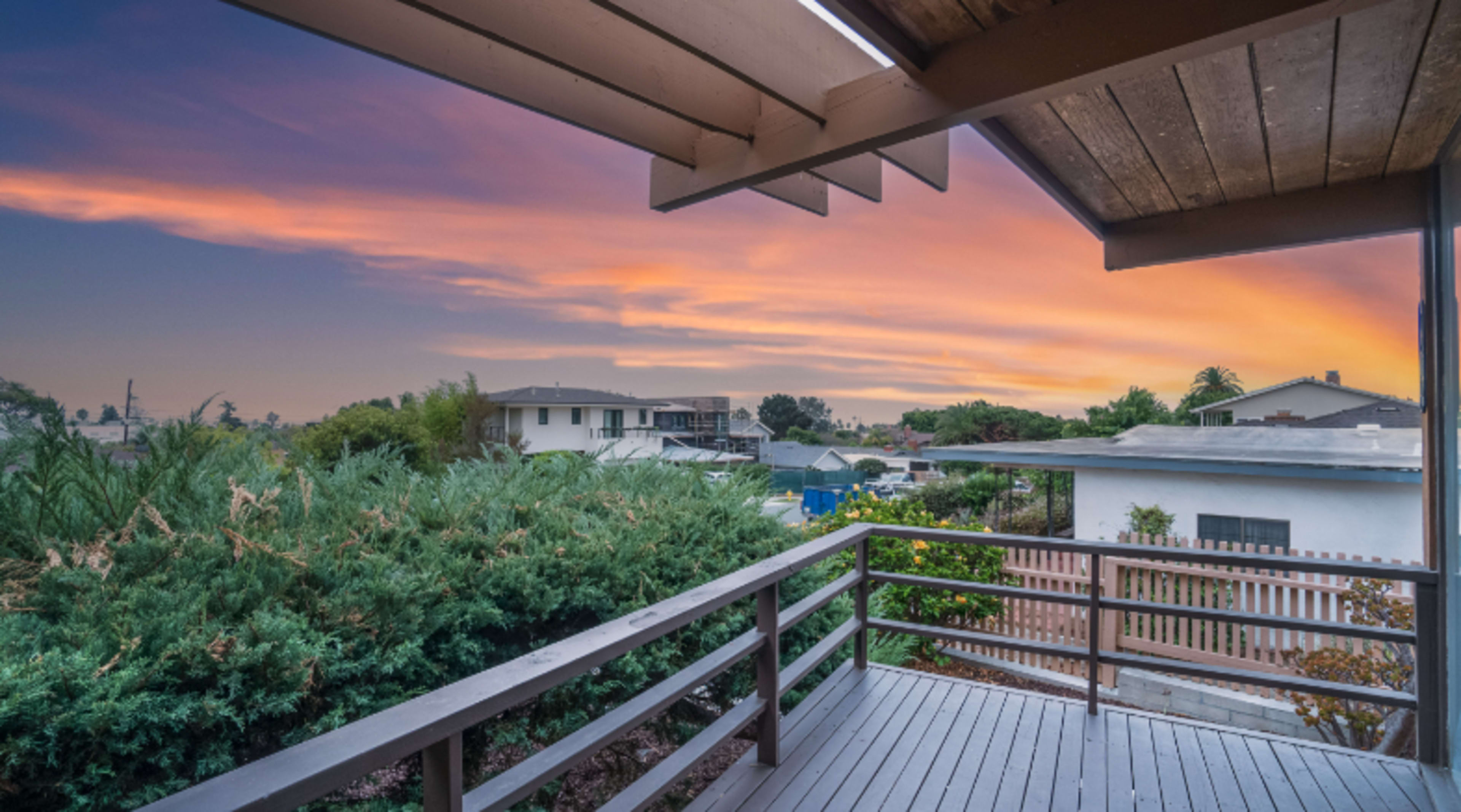 A balcony overlooking houses and greenery under a colorful sunset sky.