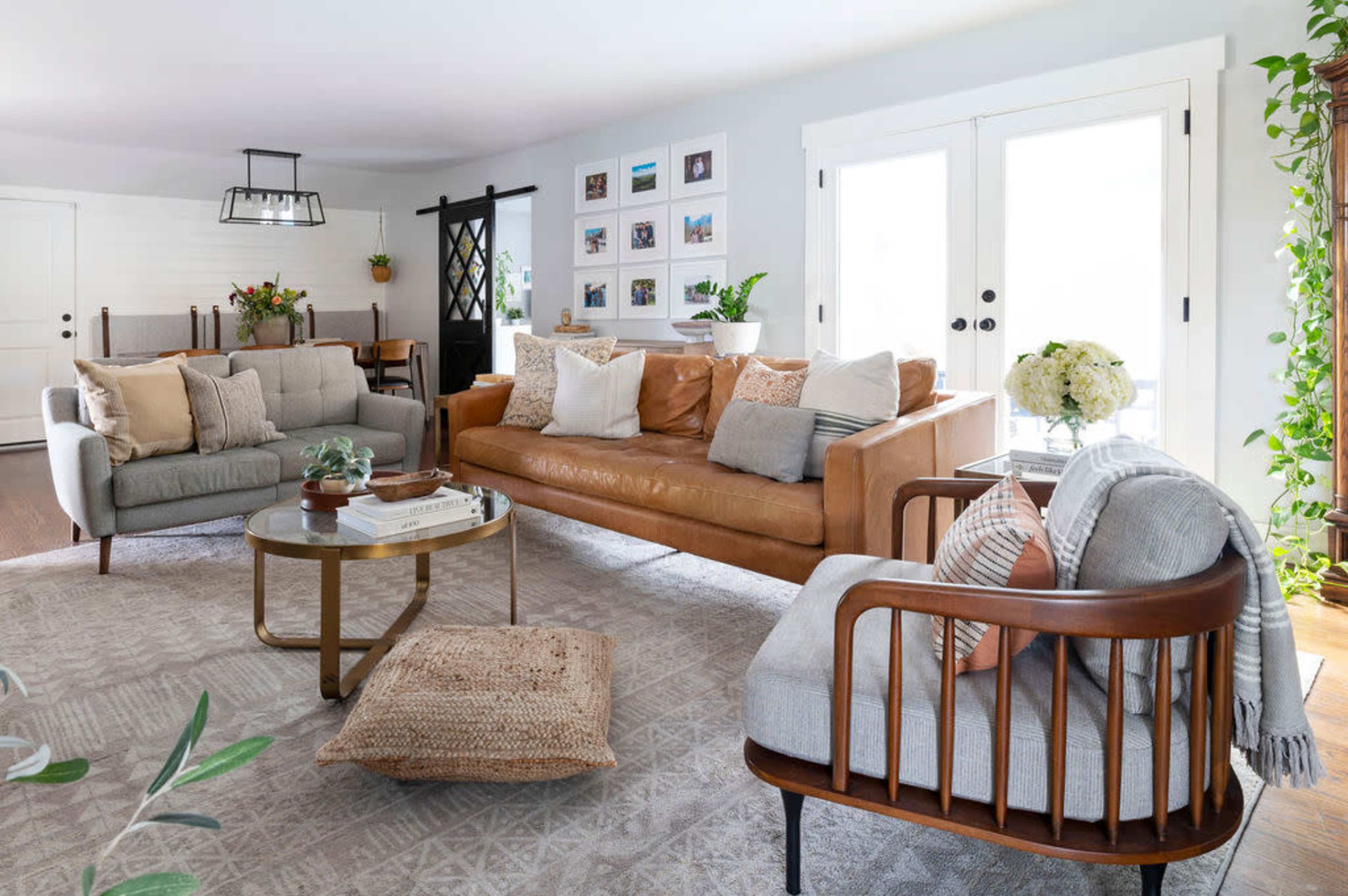 The living room features a combination of a leather sofa, two fabric chairs, a coffee table, and decorative plants, arranged around a light-colored area rug.