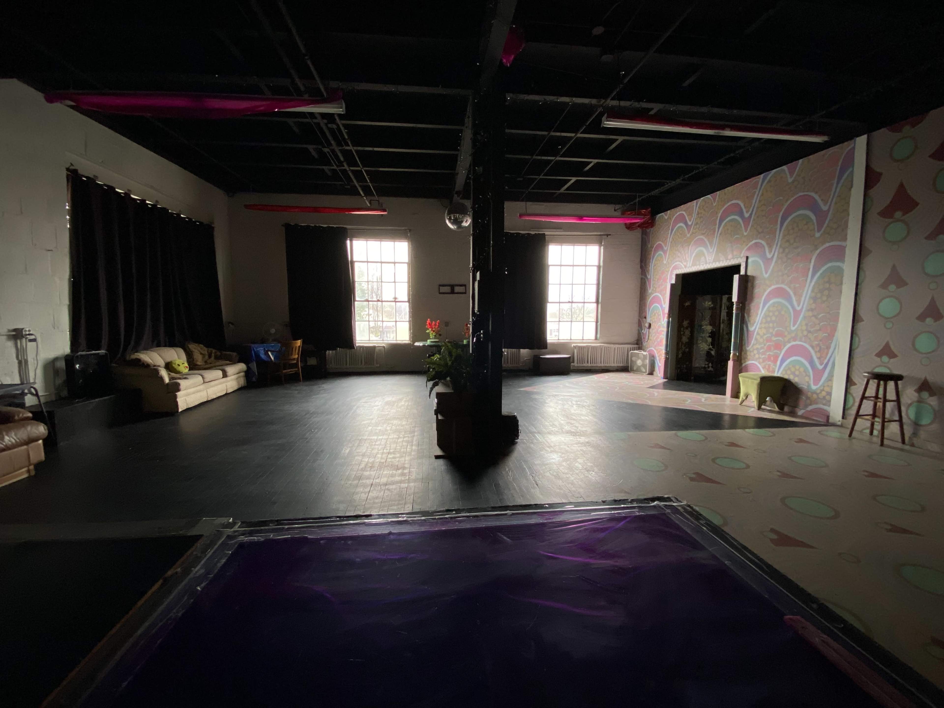 The image shows a dimly lit room featuring a patterned wall, a sofa, and a plant in the center.