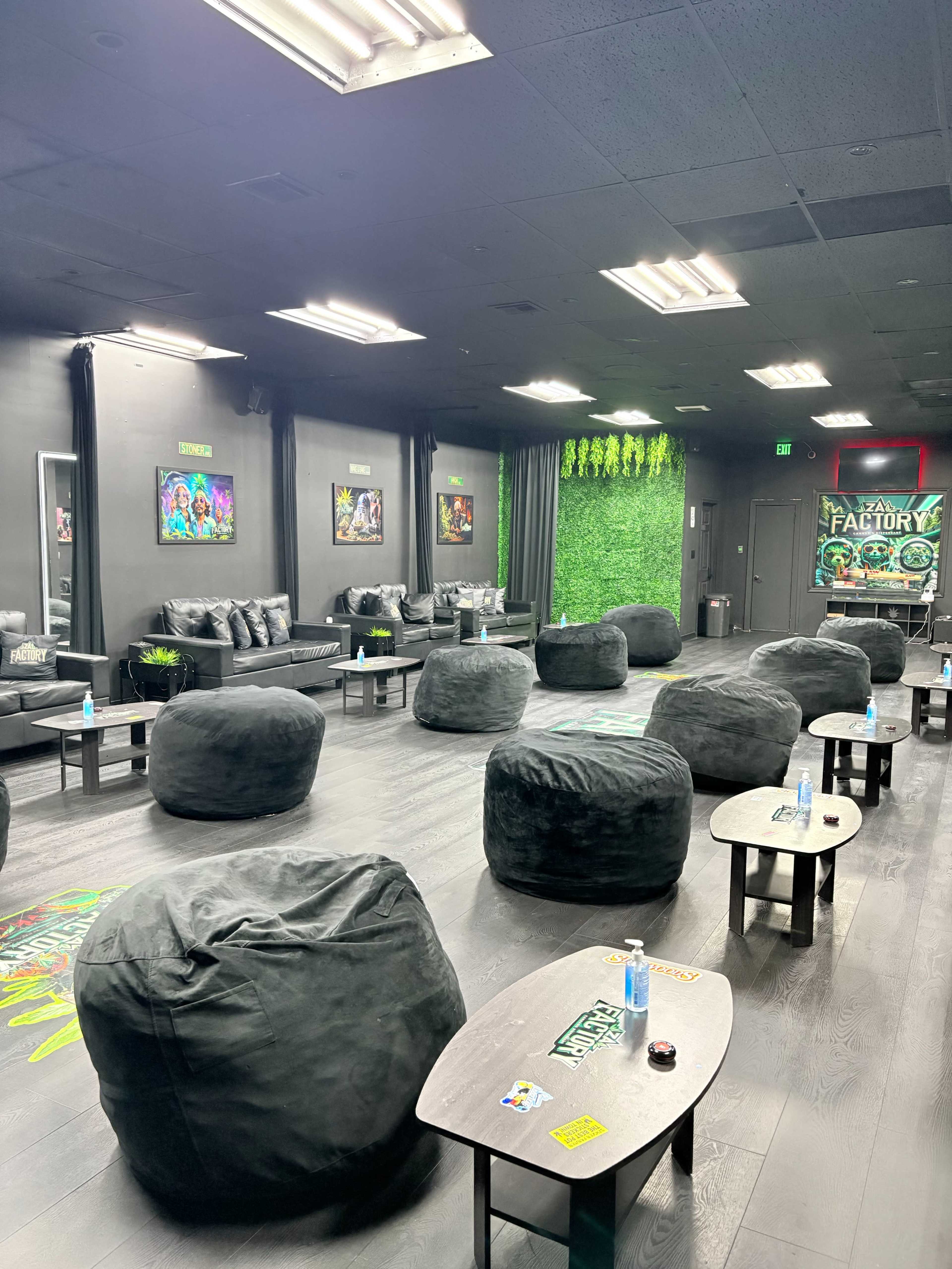 The image shows a lounge area with black bean bag chairs, small tables, and wall decorations, featuring a green plant wall and framed artwork.