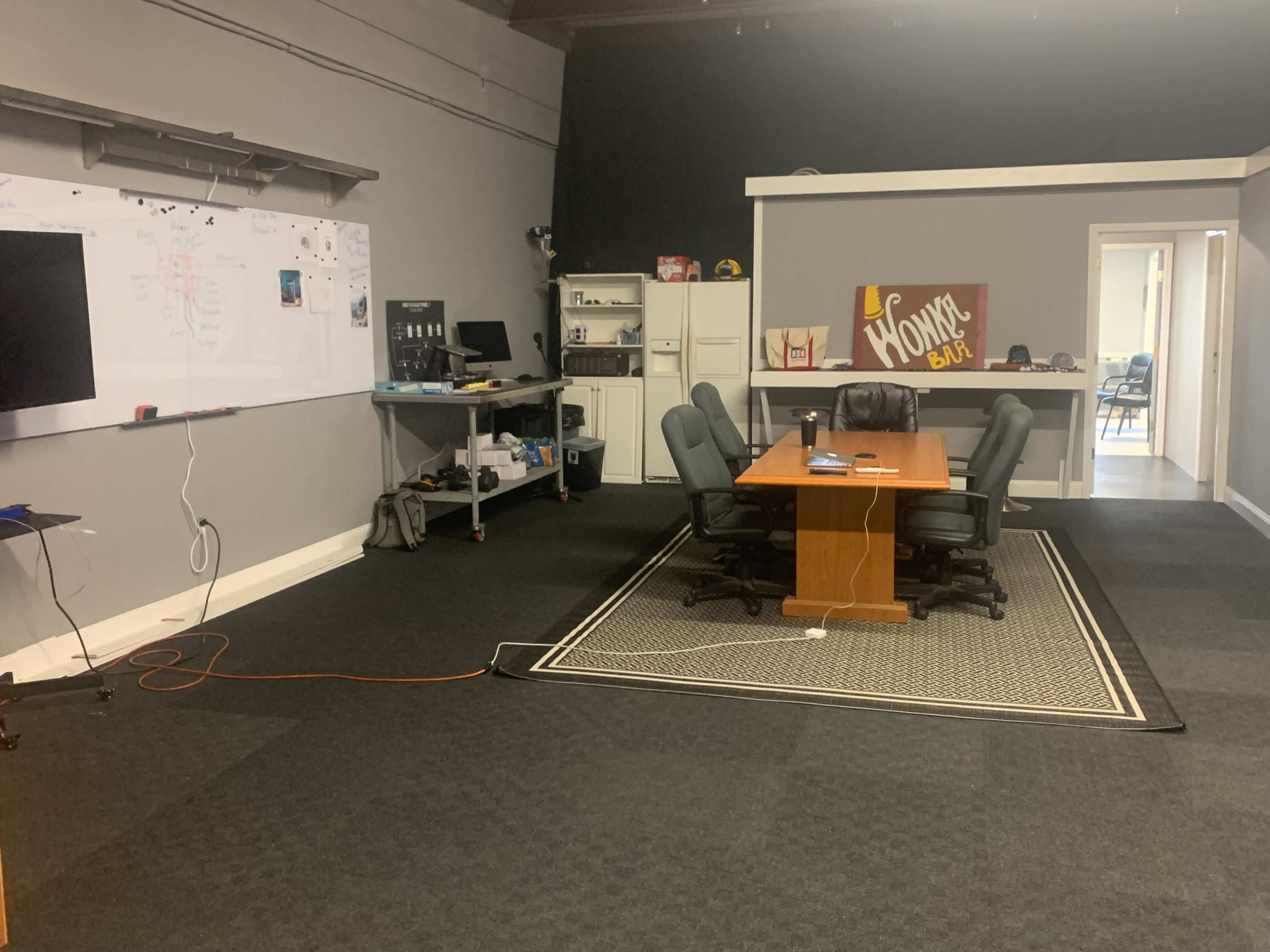 A conference room with a large wooden table surrounded by chairs, a whiteboard on the wall, and various office equipment in the background.