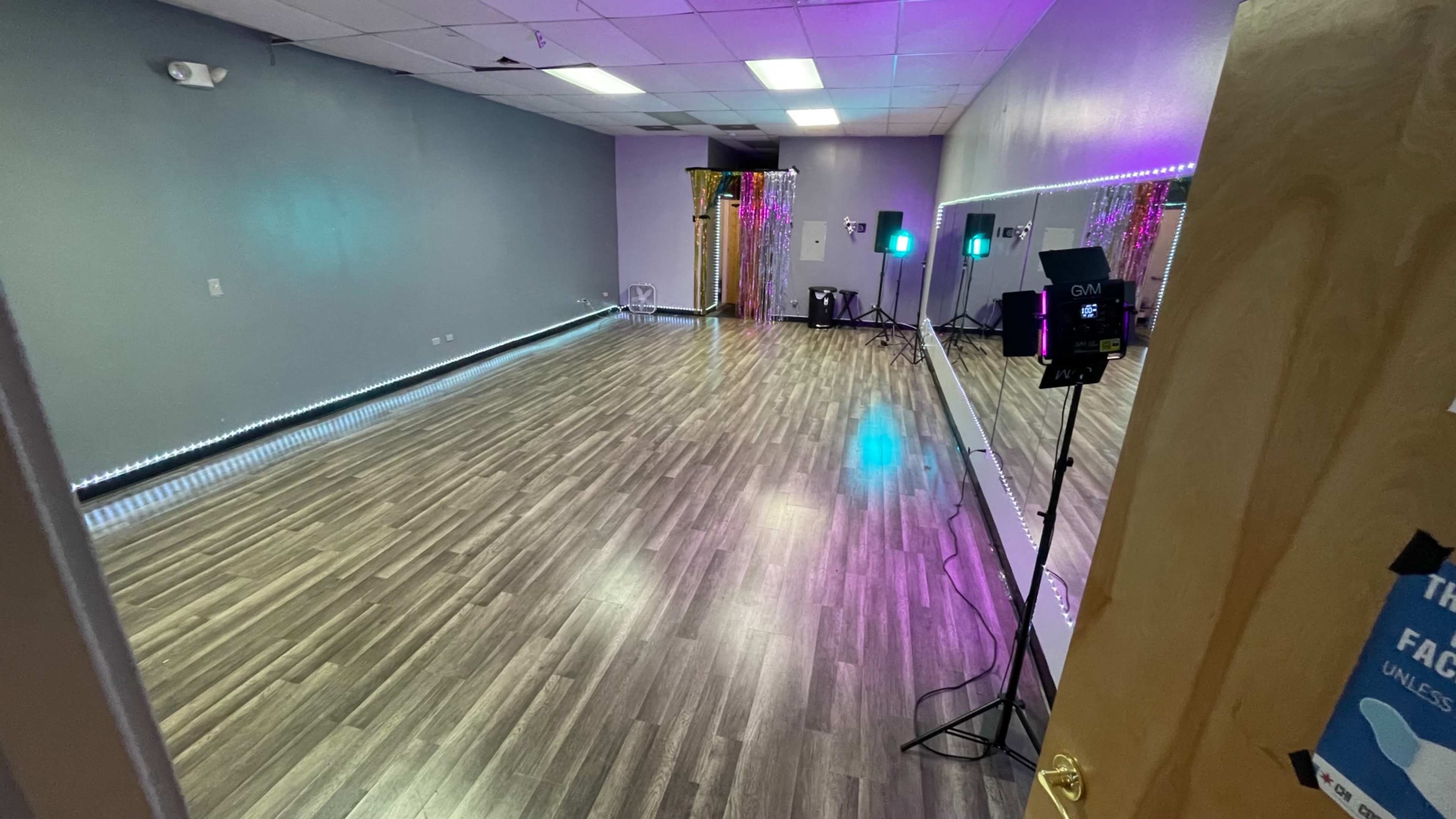 An empty dance studio with wooden flooring, mirrors on one wall, and colorful LED lights set up for events.