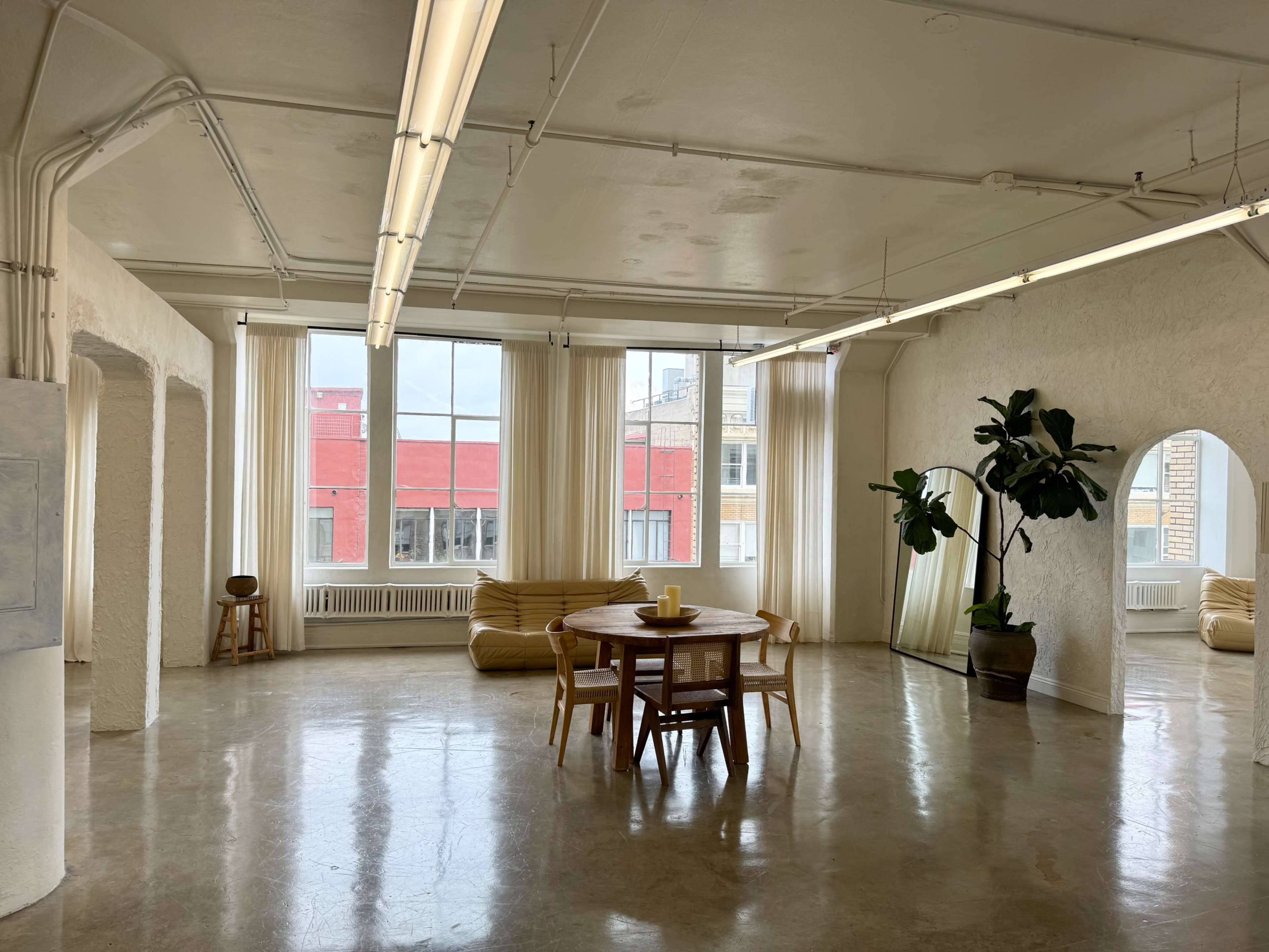 A spacious, minimalist interior with large windows, a wooden dining table, and a potted plant.
