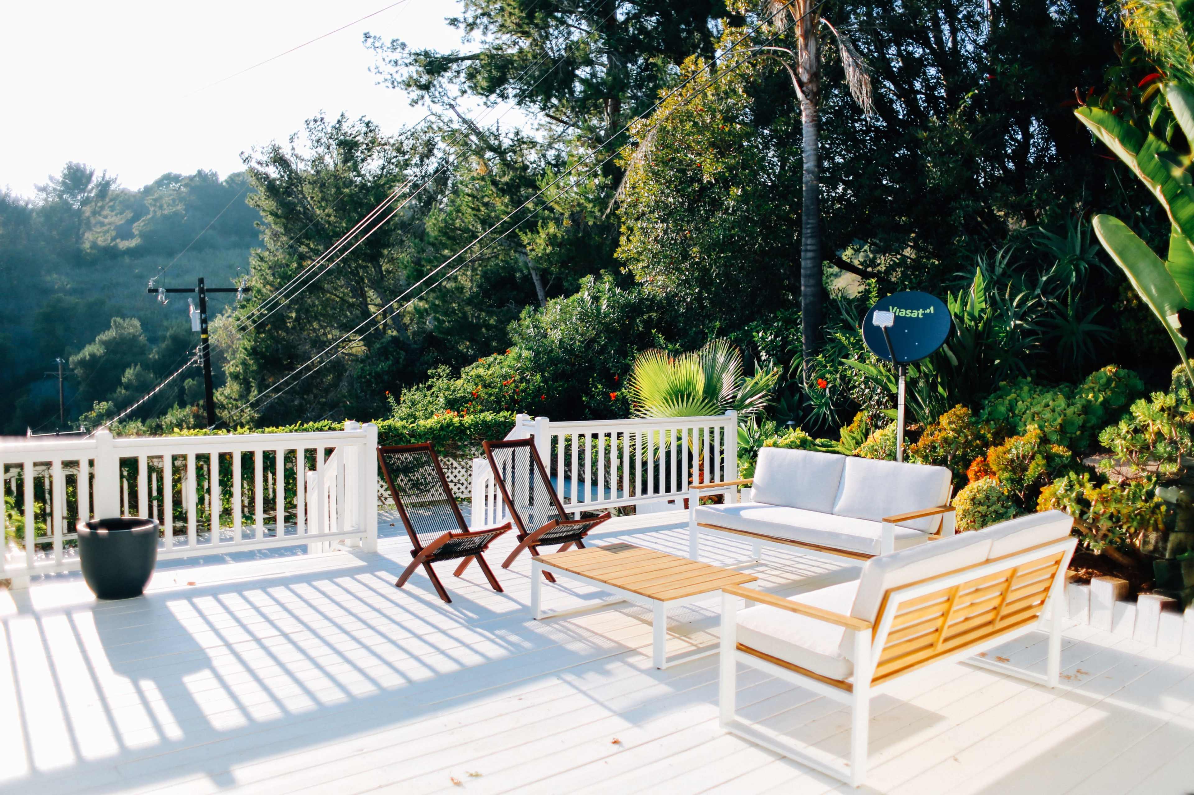 A patio with a wooden table and chairs, surrounded by greenery and overlooking a hilly landscape.