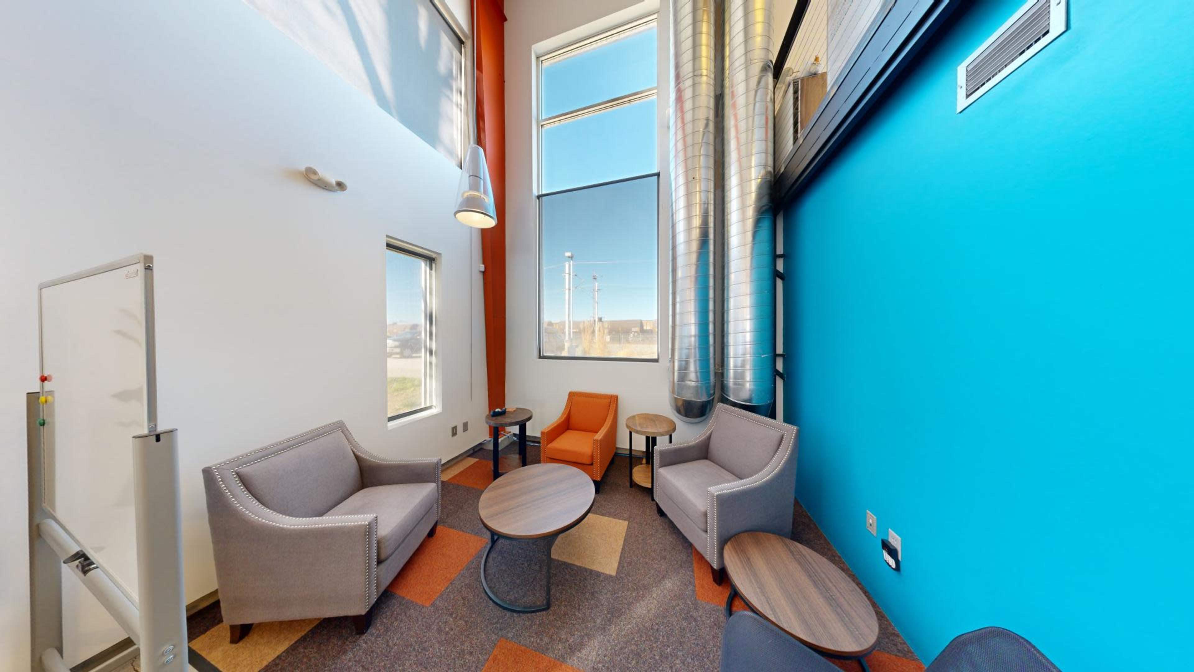 The image shows a modern seating area with chairs, a coffee table, and large windows allowing natural light to enter.