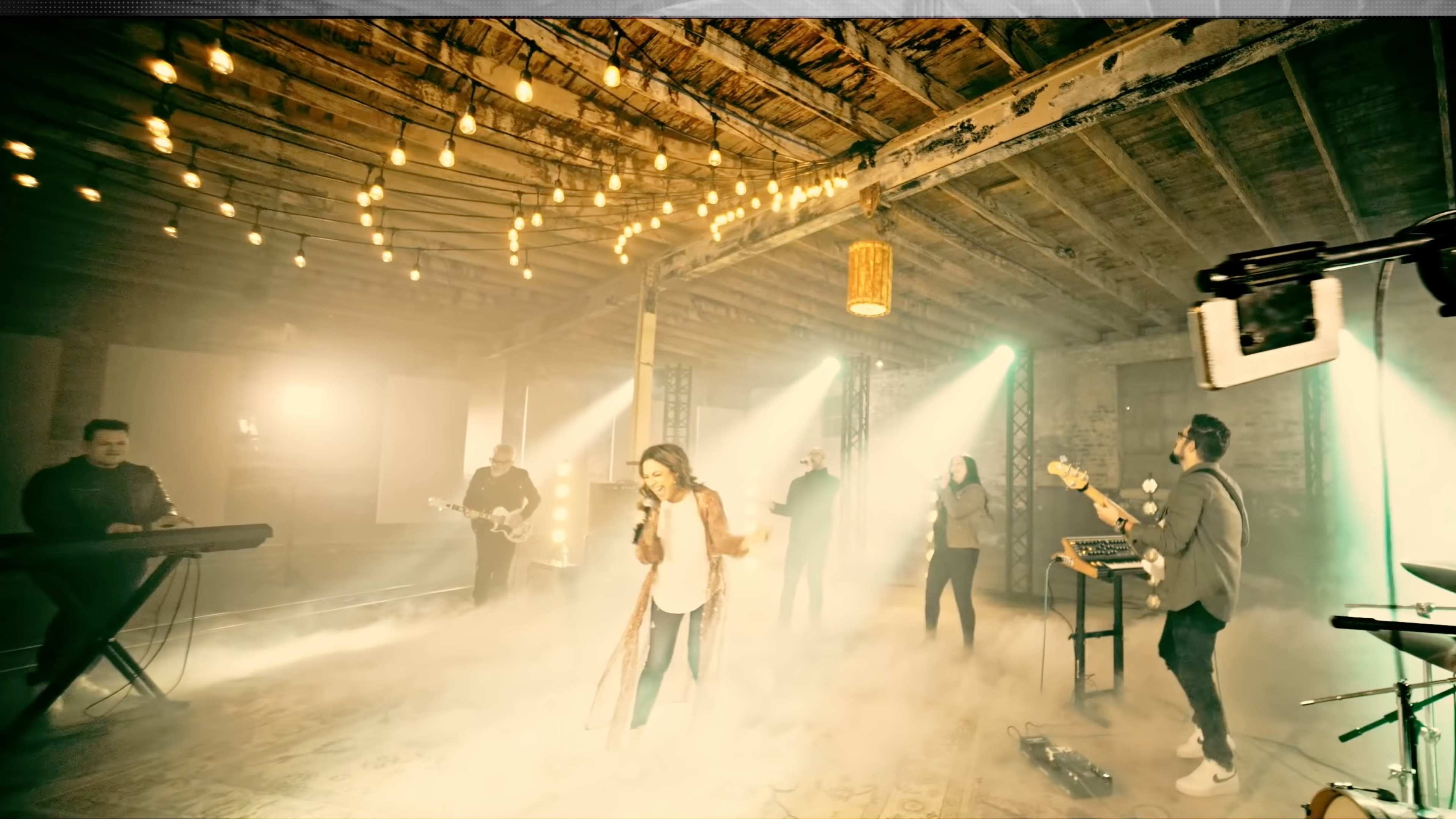 A band performs in a dimly lit, hazy venue with string lights hanging from the ceiling.