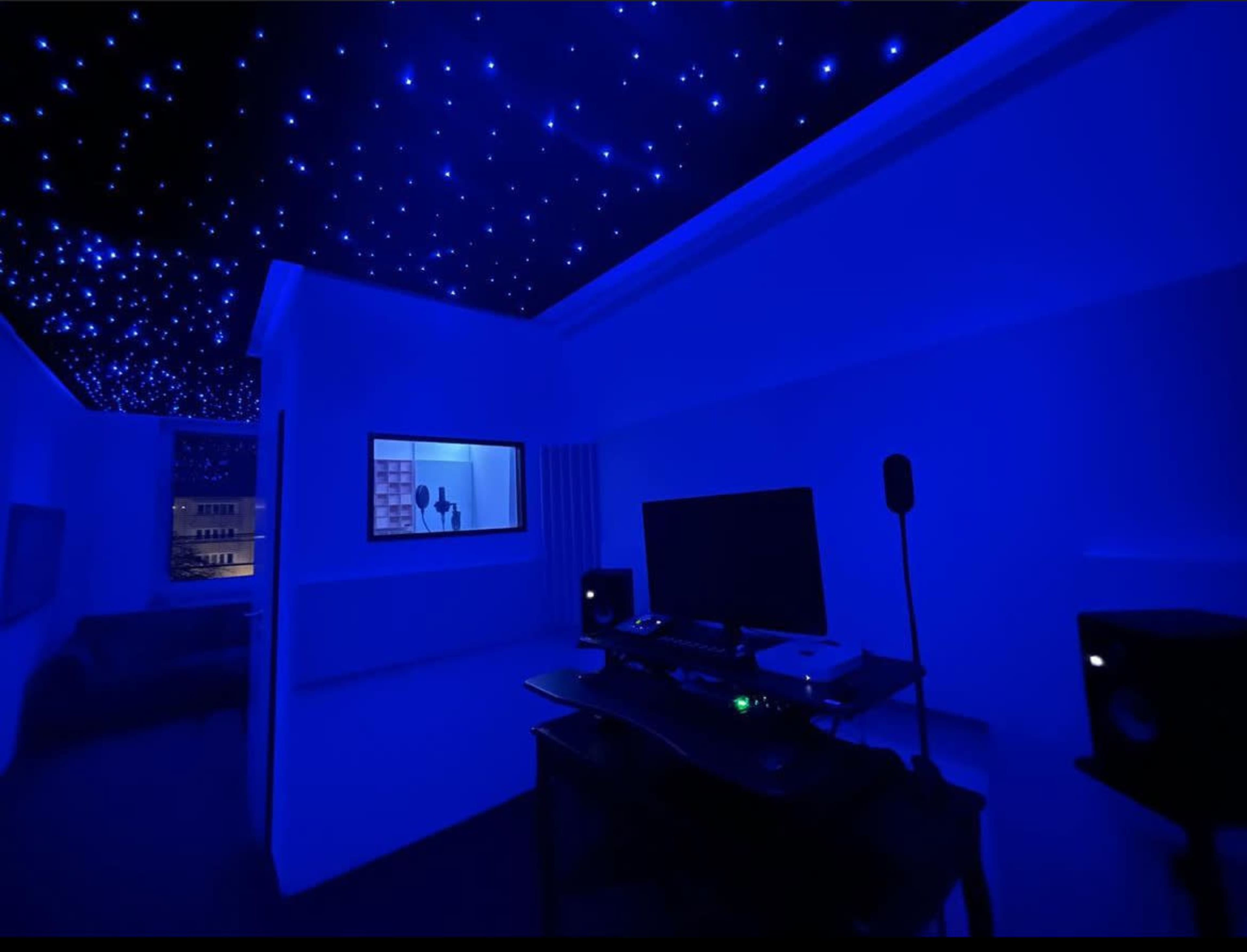 The room features a blue-lit interior with a starry ceiling, a large monitor on a desk, and a person visible through a window.