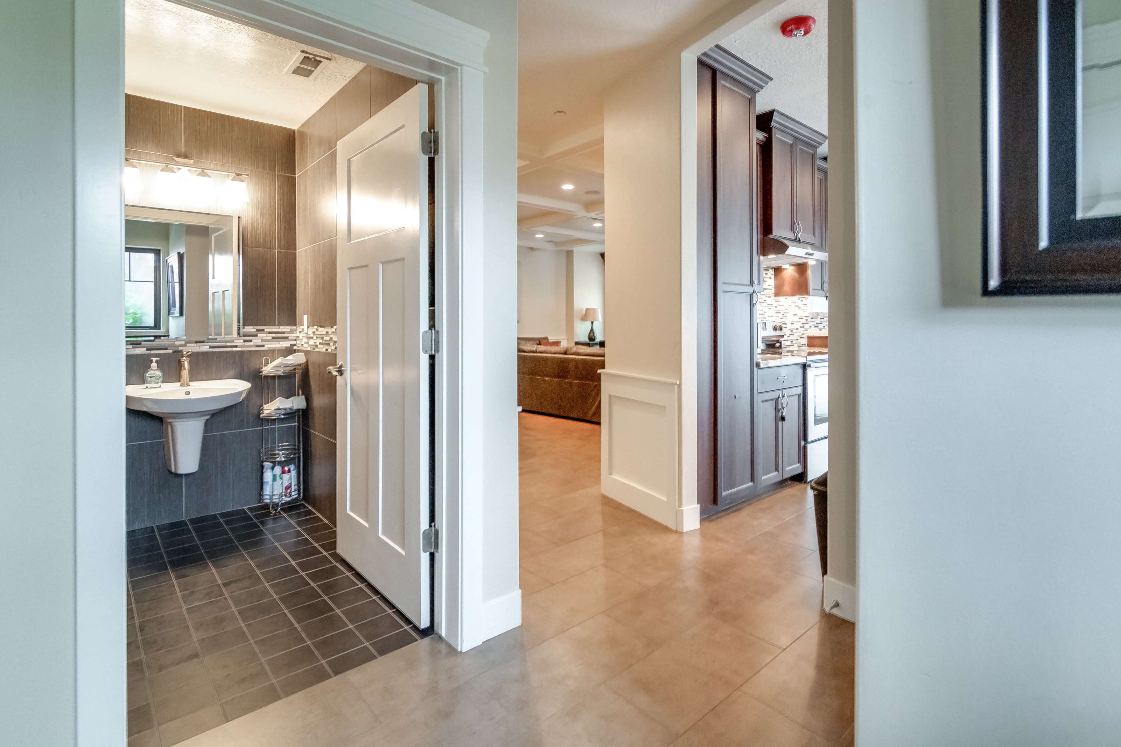 A view from a hallway leading into a bathroom on the left and a kitchen area on the right, with a living room visible in the distance.