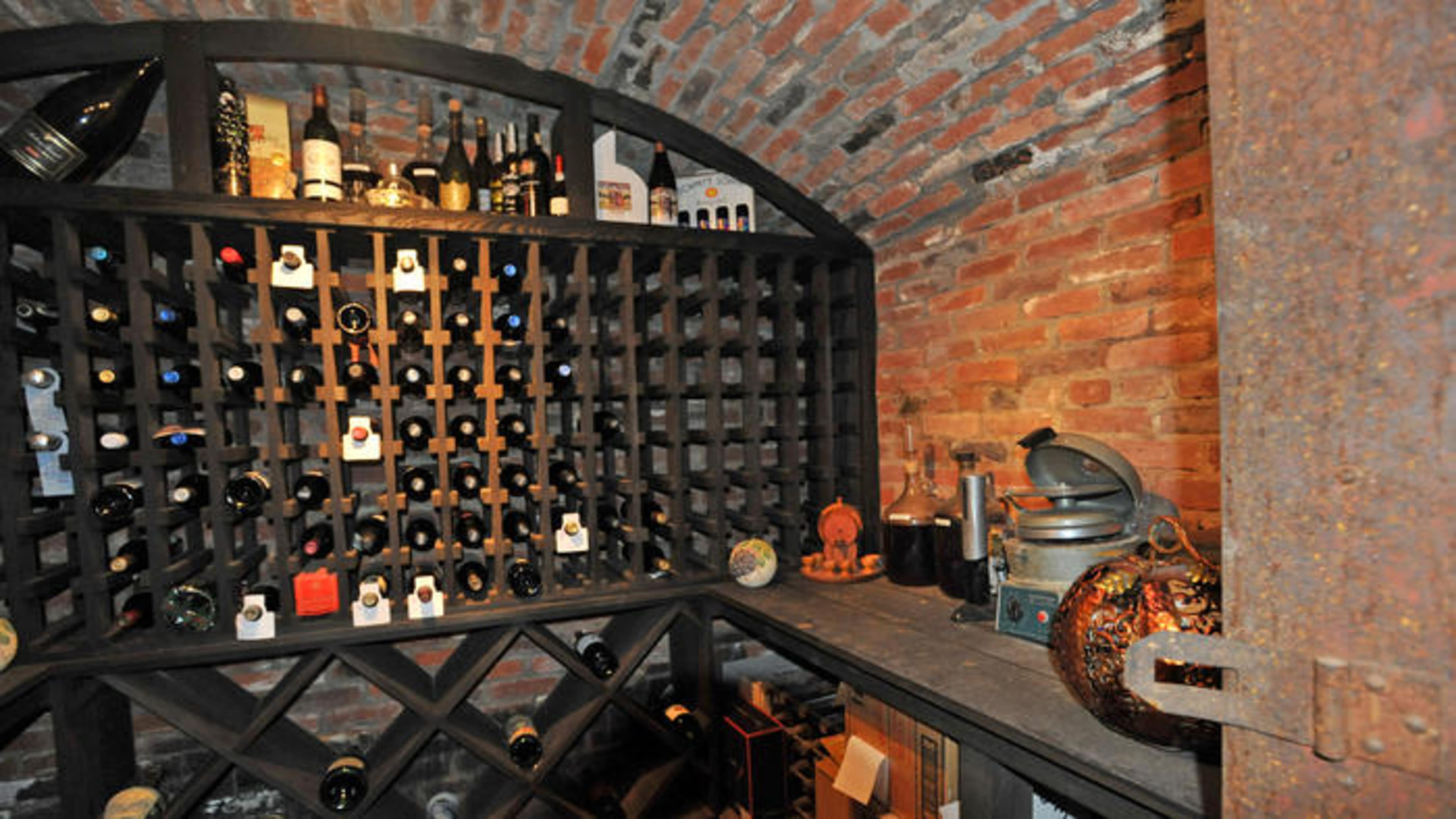 A brick wine cellar with a wooden wine rack filled with bottles and a small table with wine accessories.