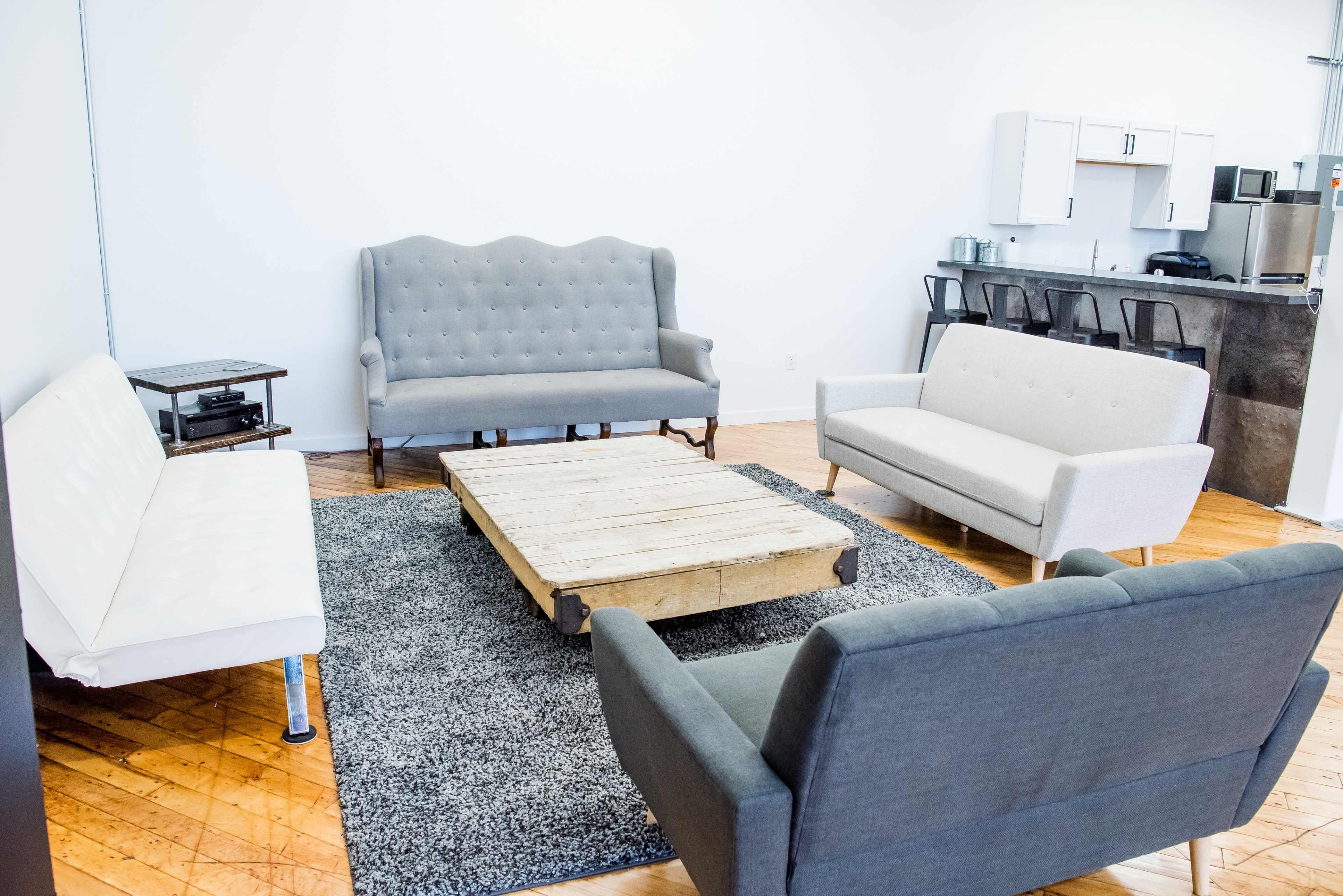 A modern lounge area with three sofas and a wooden coffee table on a gray rug.