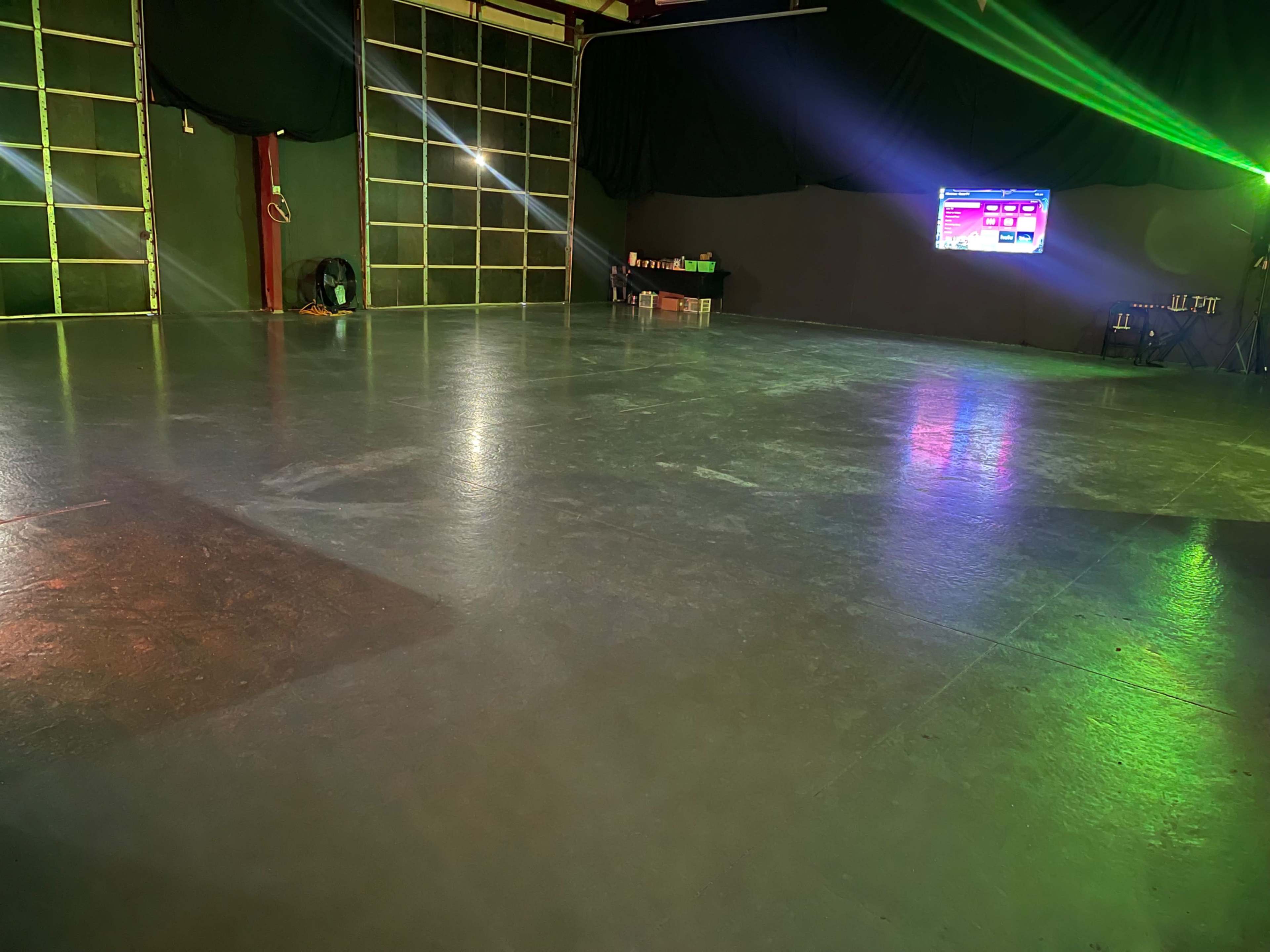 A large, empty dance studio with a polished floor, ambient lighting, and a screen displaying content in the background.