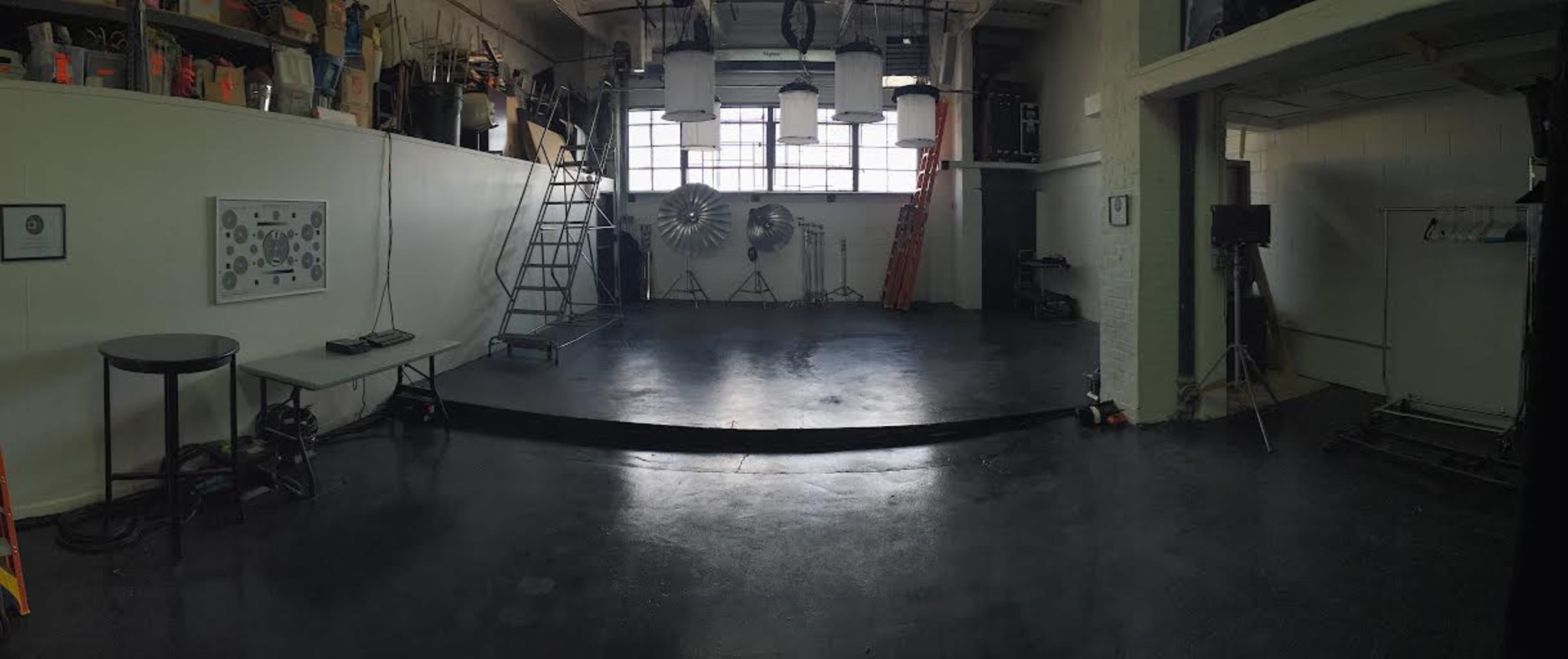 A large, empty studio space with a polished floor, lighting equipment, and various props arranged along the walls.