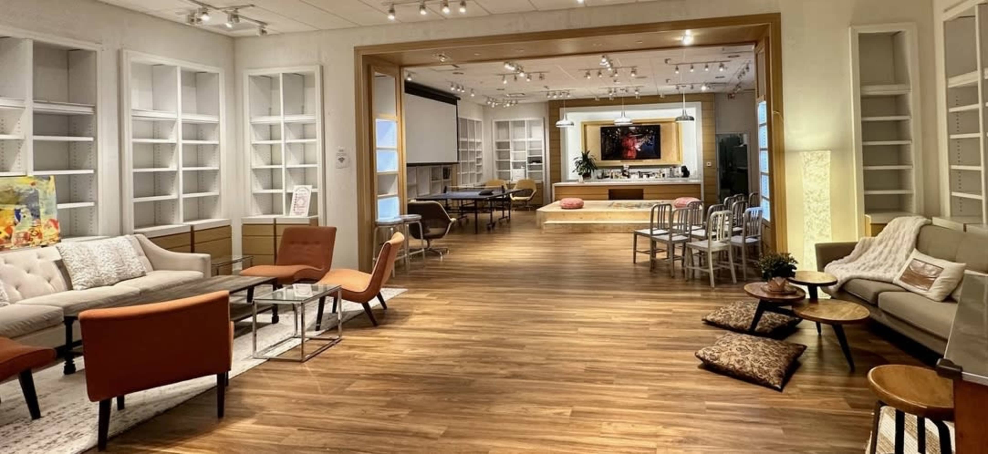 A well-lit interior space featuring a living area with sofas and armchairs, a dining area with tables and chairs, and a versatile layout with wooden flooring.