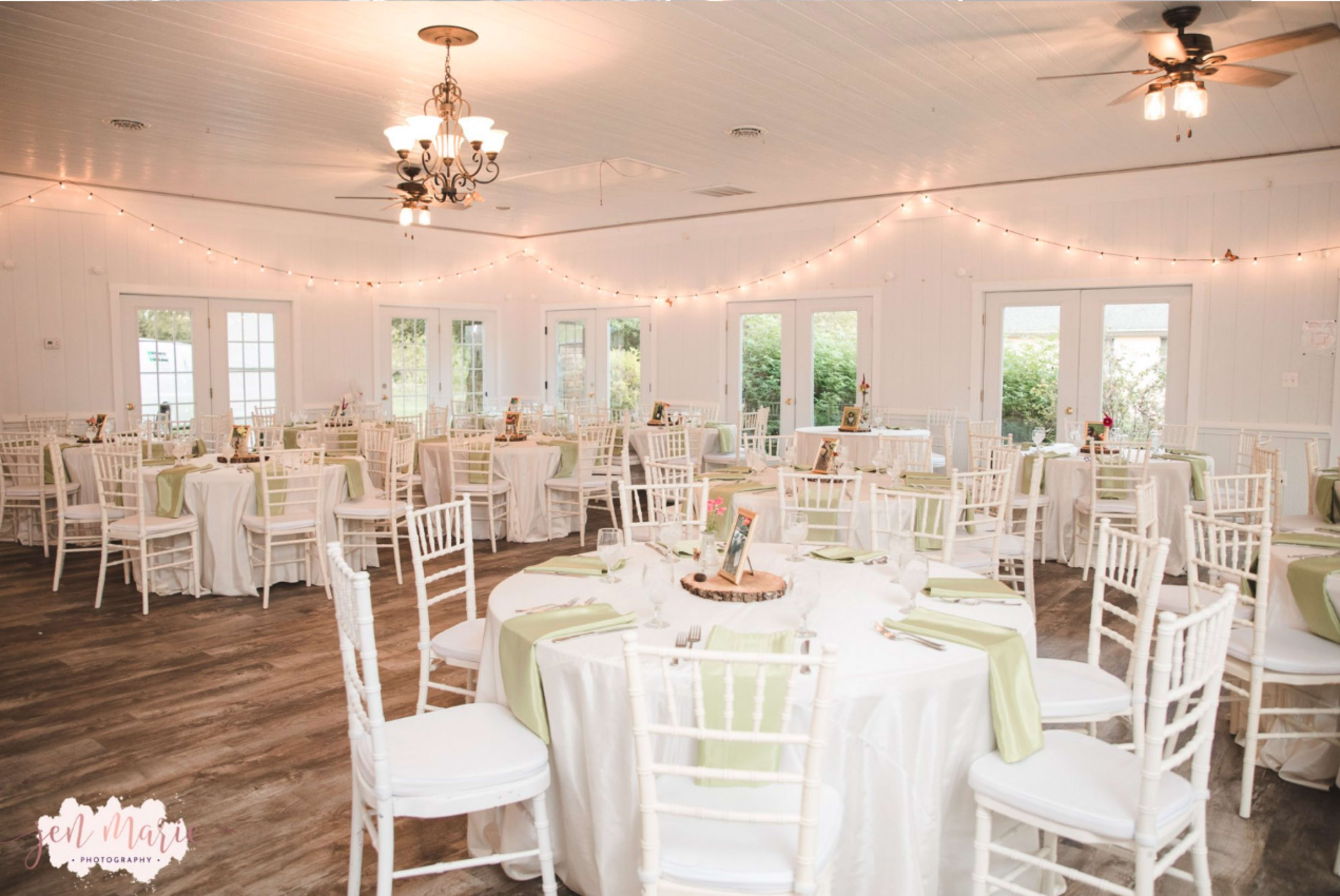 A well-decorated event space featuring round tables with white tablecloths and green accents, surrounded by white chairs and illuminated by soft lighting.