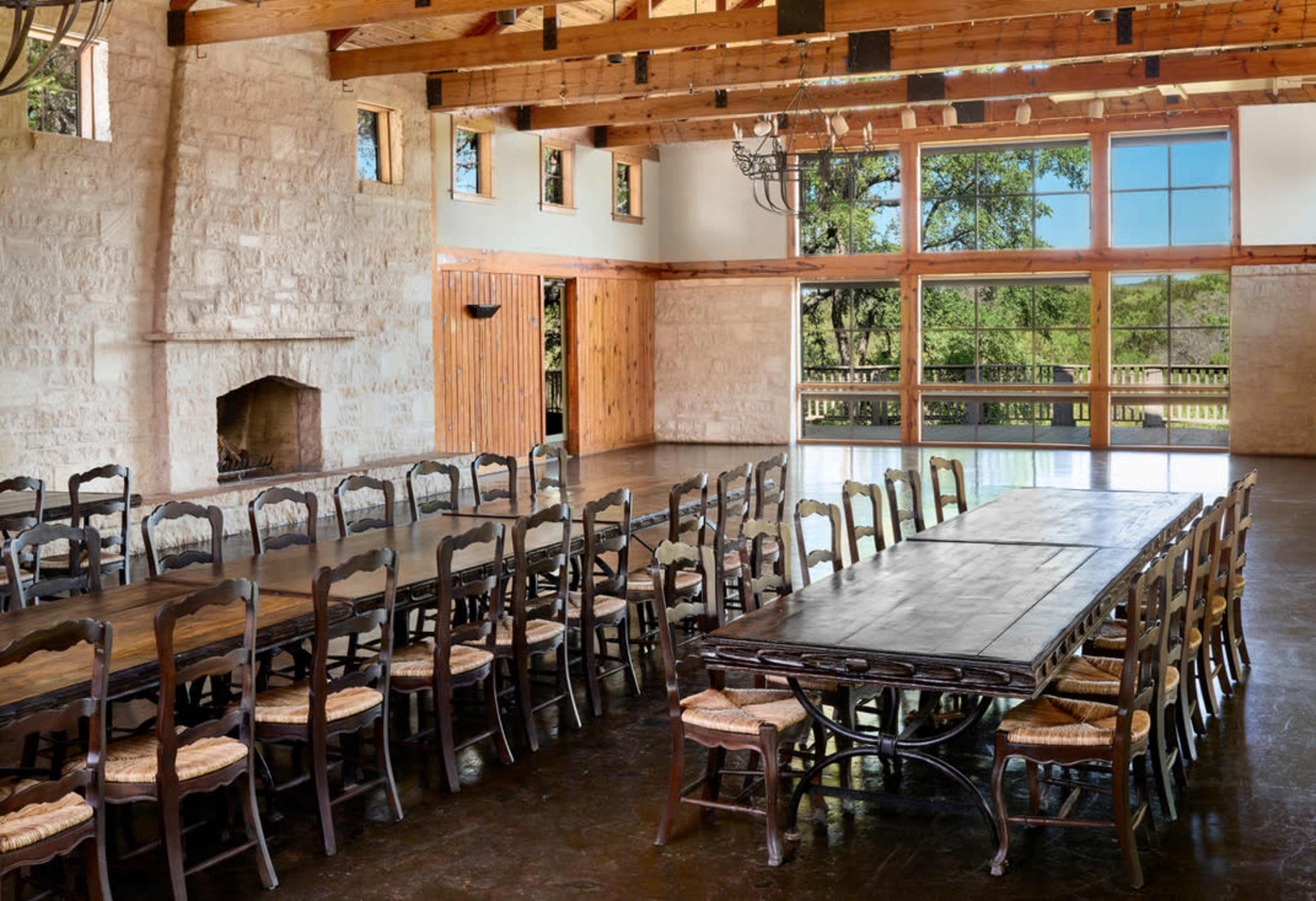 The image shows a spacious banquet hall with wooden beams, large windows, and long dining tables arranged with chairs.