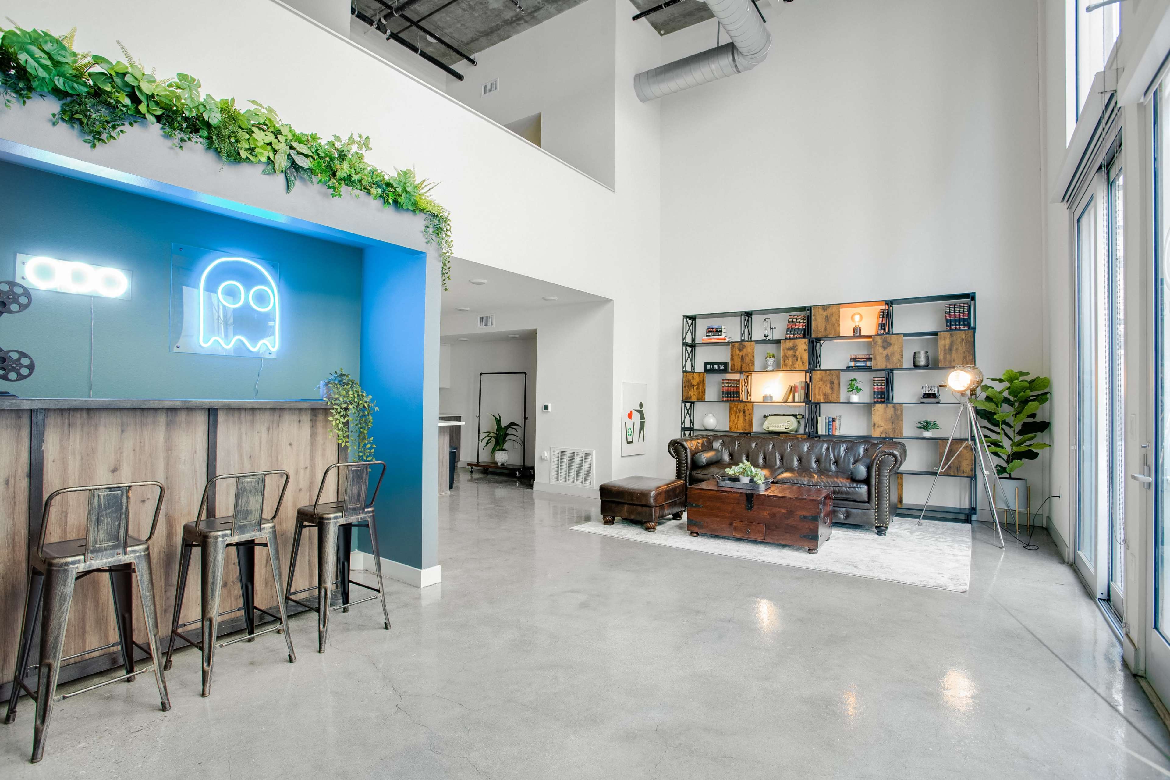 A modern lobby area featuring a bar with high stools on one side and a lounge area with a leather couch and shelves displaying various decorative items on the other.