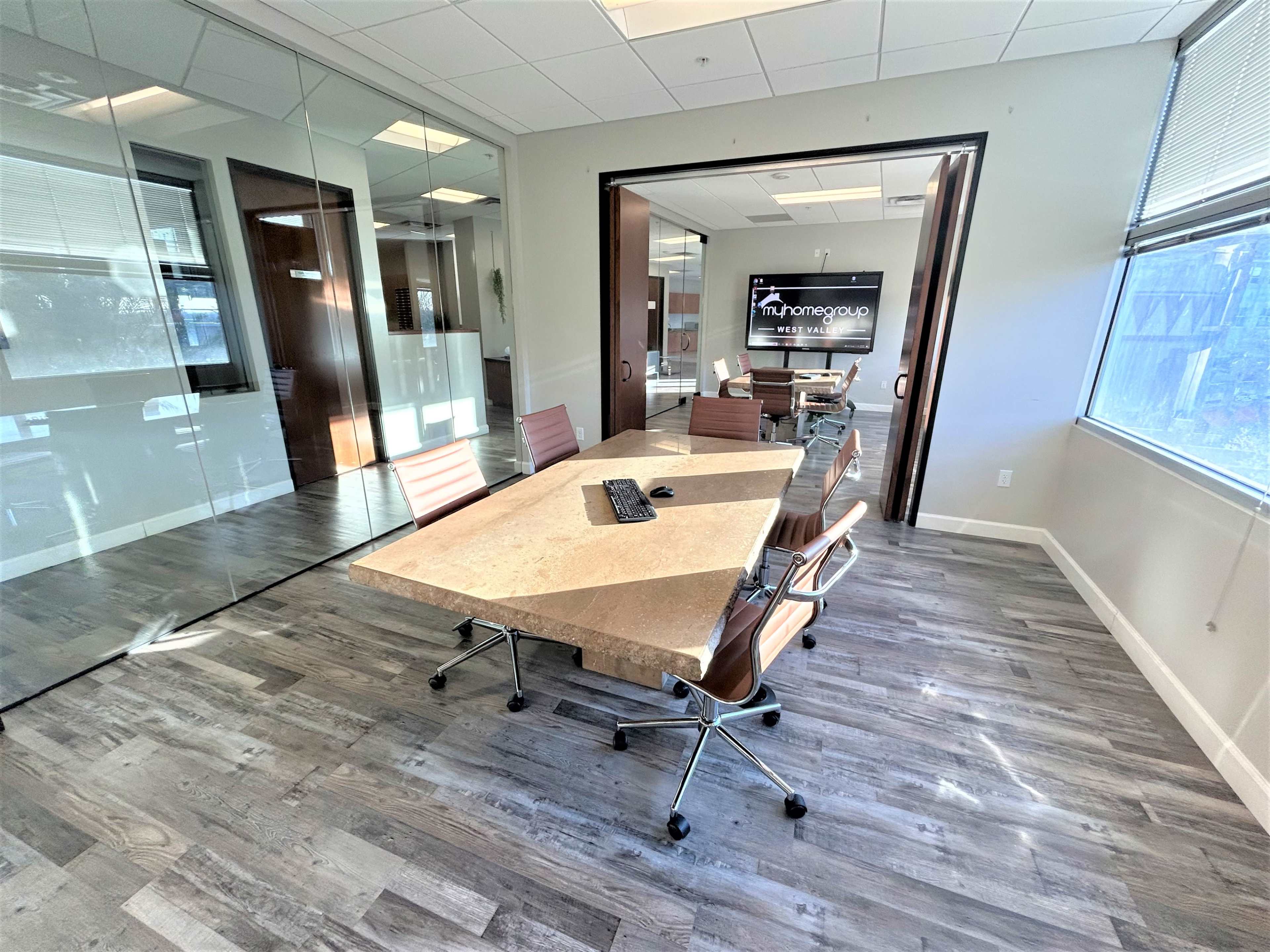 A modern conference room features a large stone table surrounded by ergonomic chairs and a wall-mounted screen.