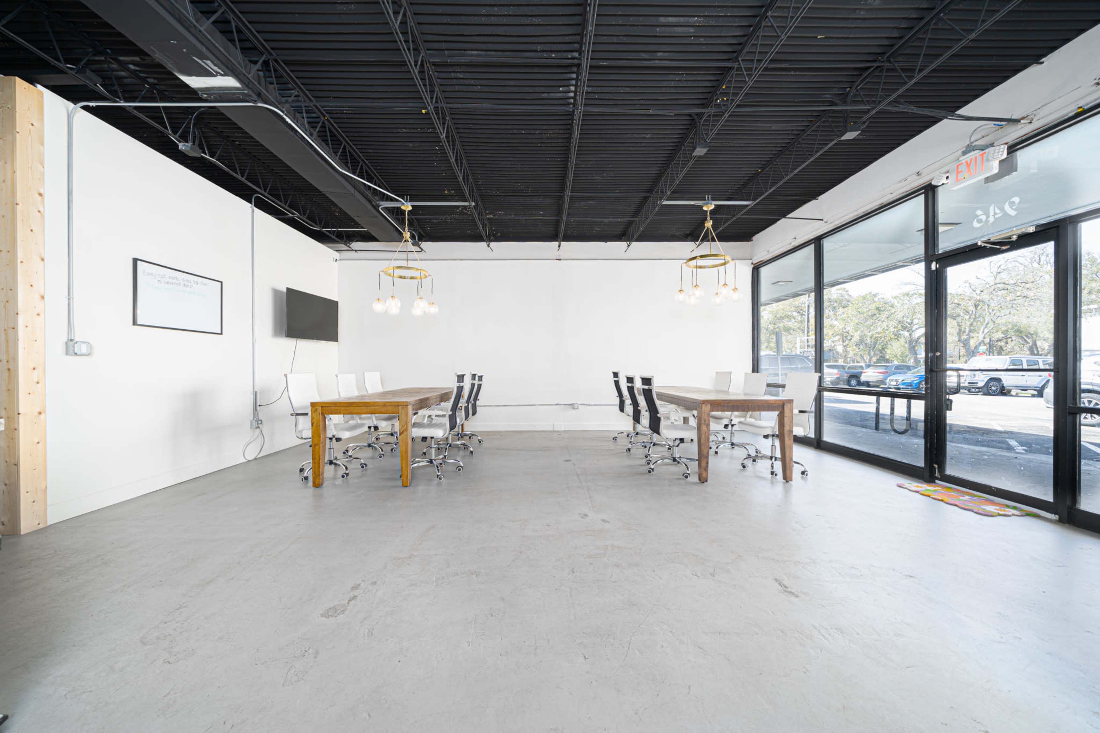 The image shows a spacious, modern conference room with a large wooden table surrounded by chairs, and glass doors leading to an outdoor area.