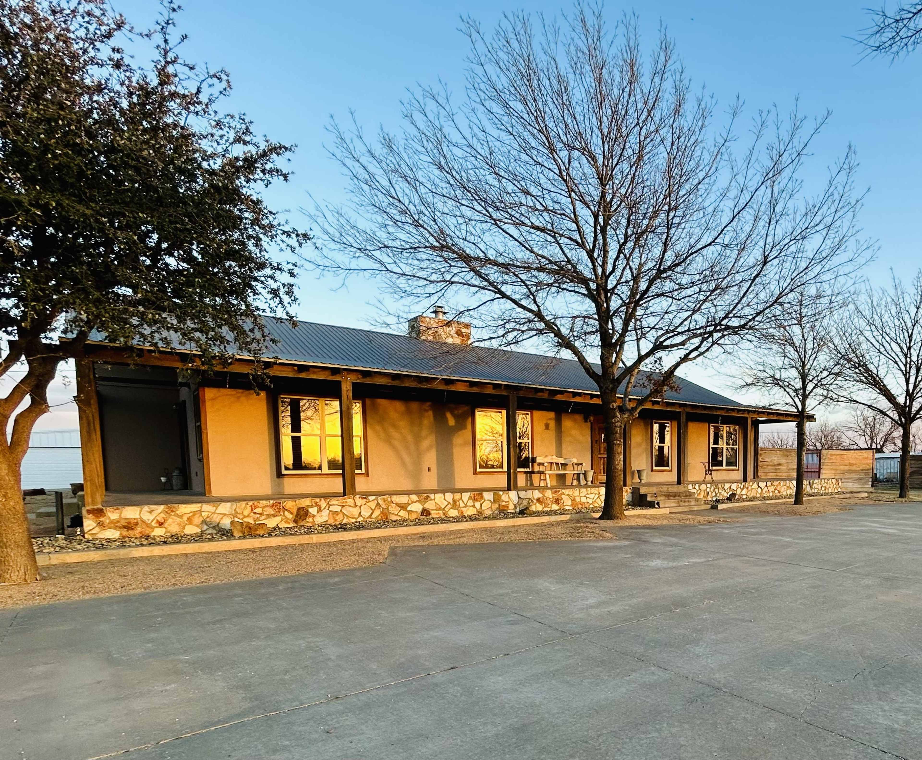 A single-story building with a stone foundation and a metal roof is surrounded by bare trees and a gravel driveway.