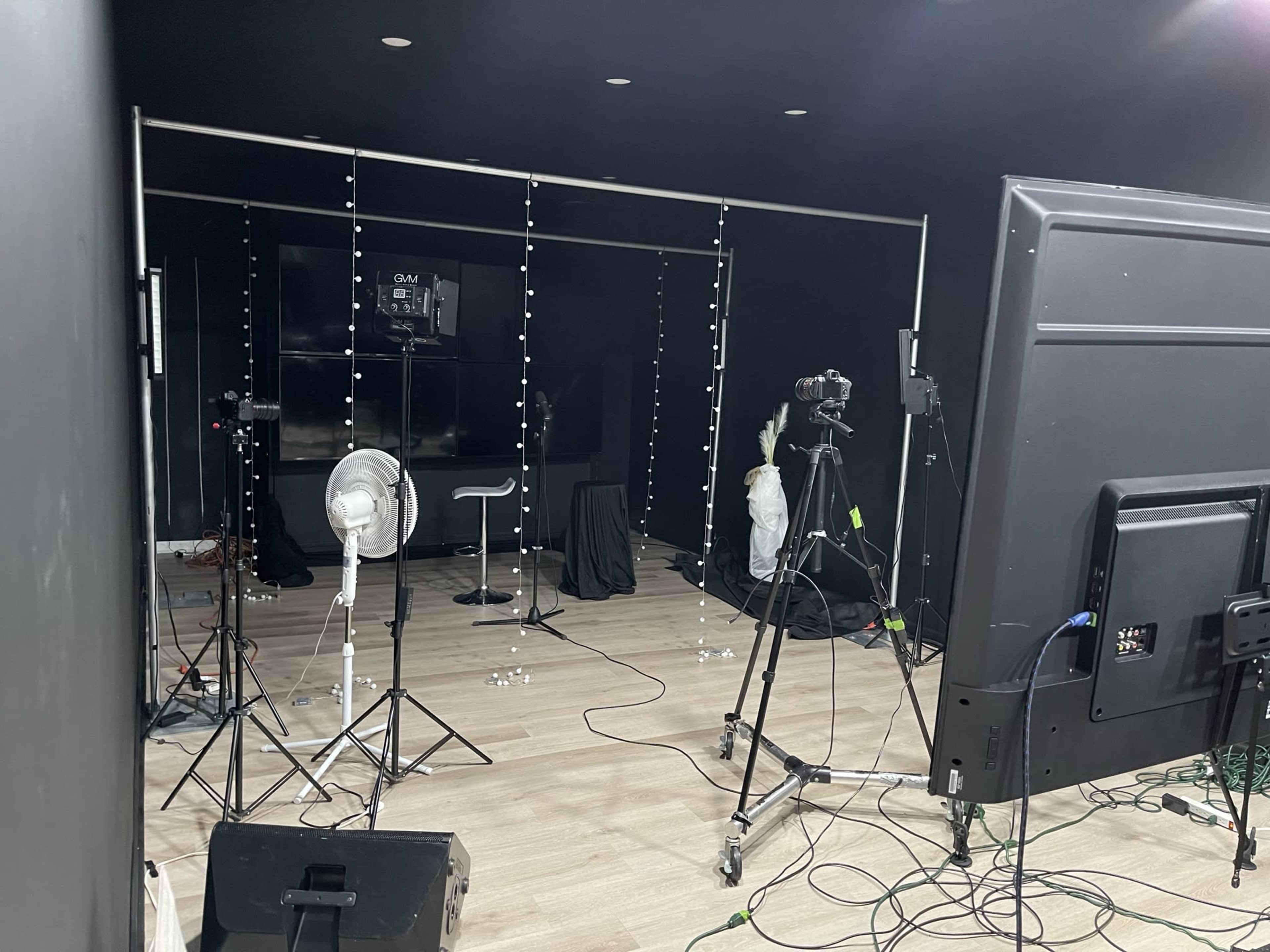 A photography studio setup with cameras, lighting equipment, and a backdrop of black curtains.