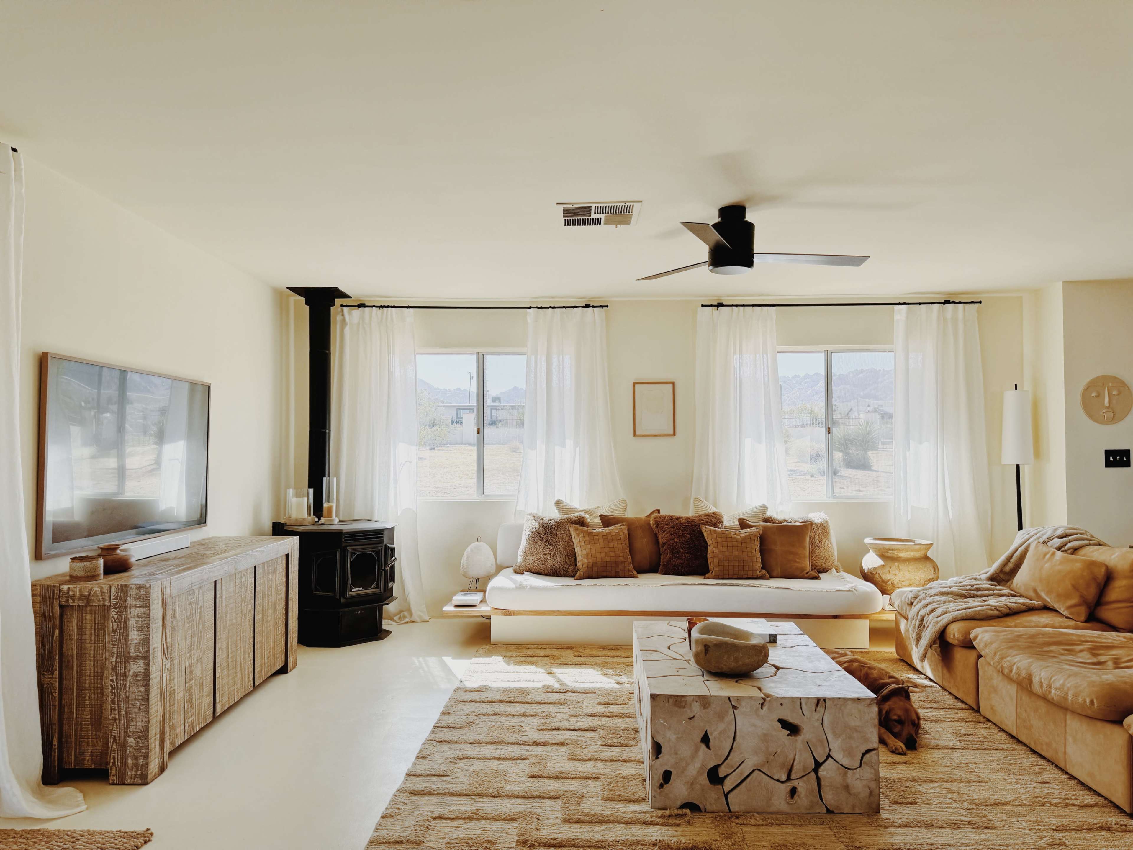 The living room features a sectional sofa and a wooden coffee table, with large windows allowing natural light to fill the space.