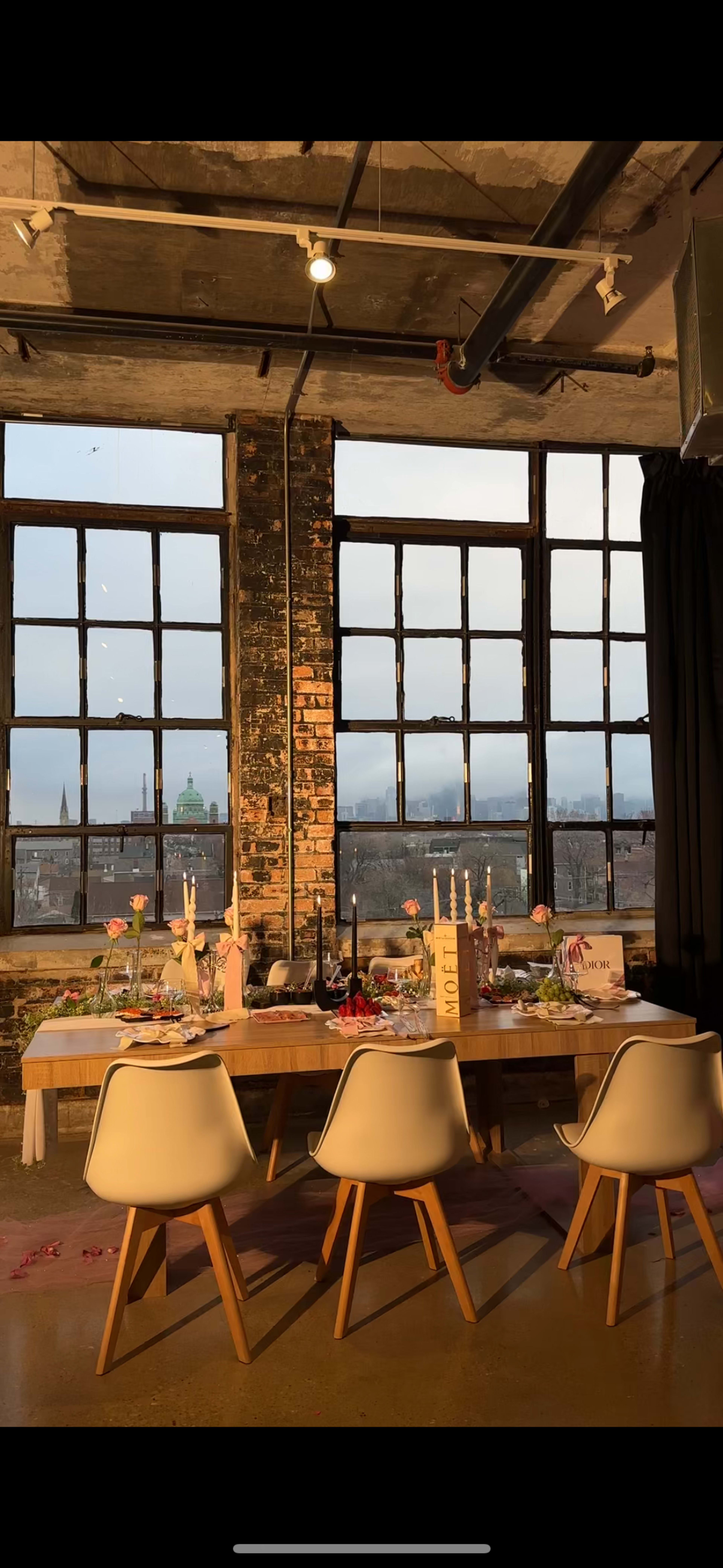 A dining table is set with food and decorations in front of large windows overlooking a cityscape.