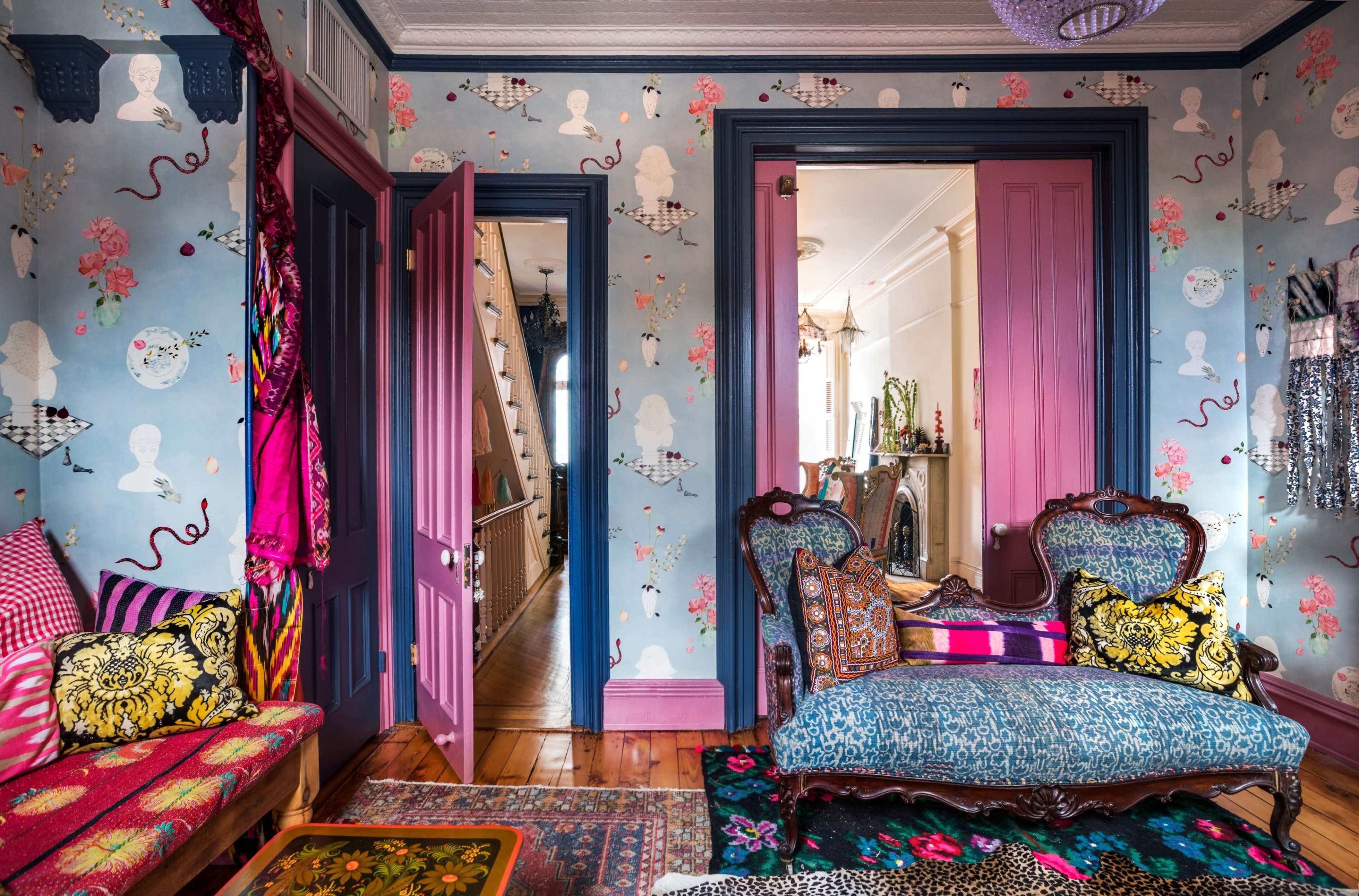 The image shows a vibrant room with patterned wallpaper, colorful furniture, and a view into a hallway adorned with decorative elements.