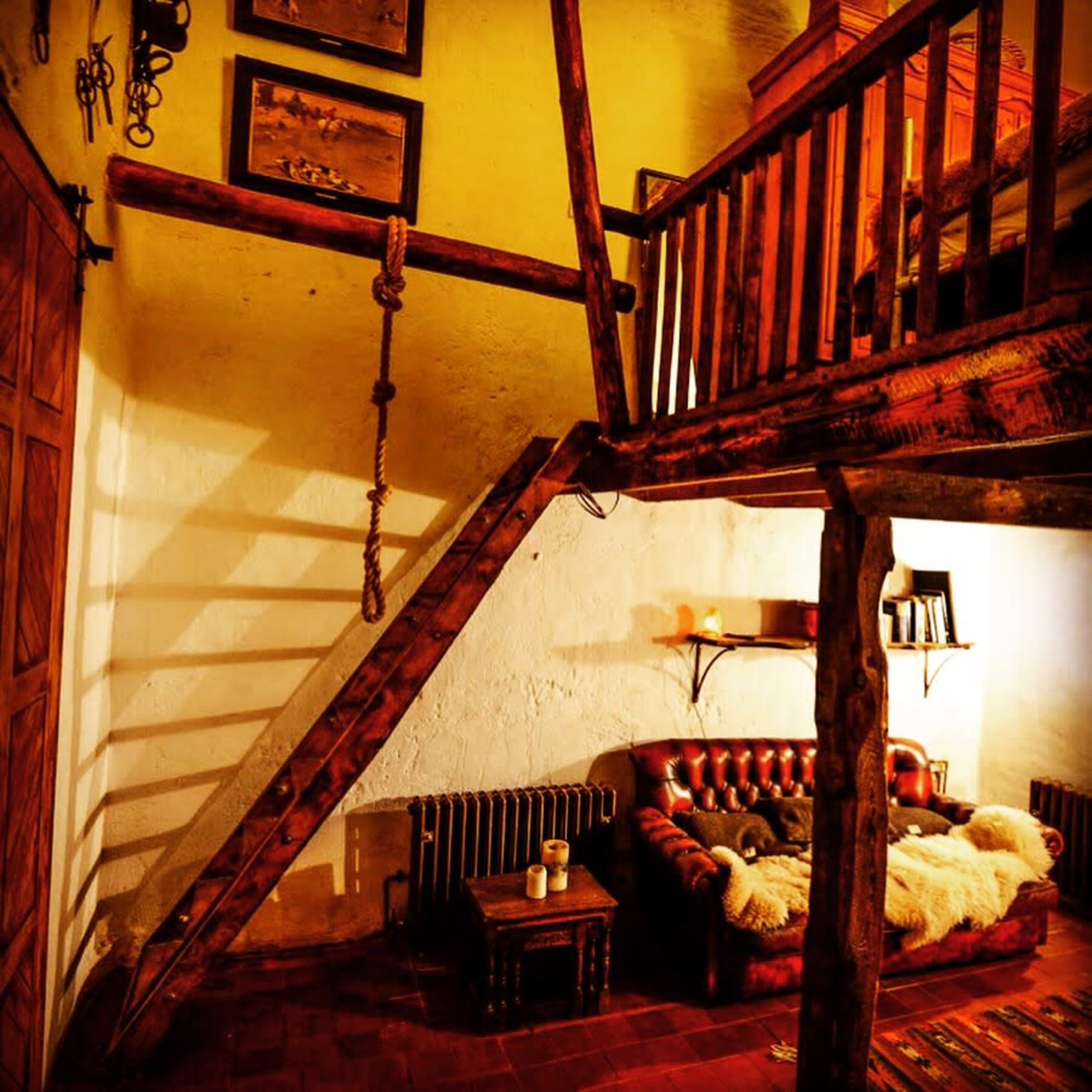 A rustic living room with a wooden staircase leading to a loft area, featuring a leather couch and a cozy rug.