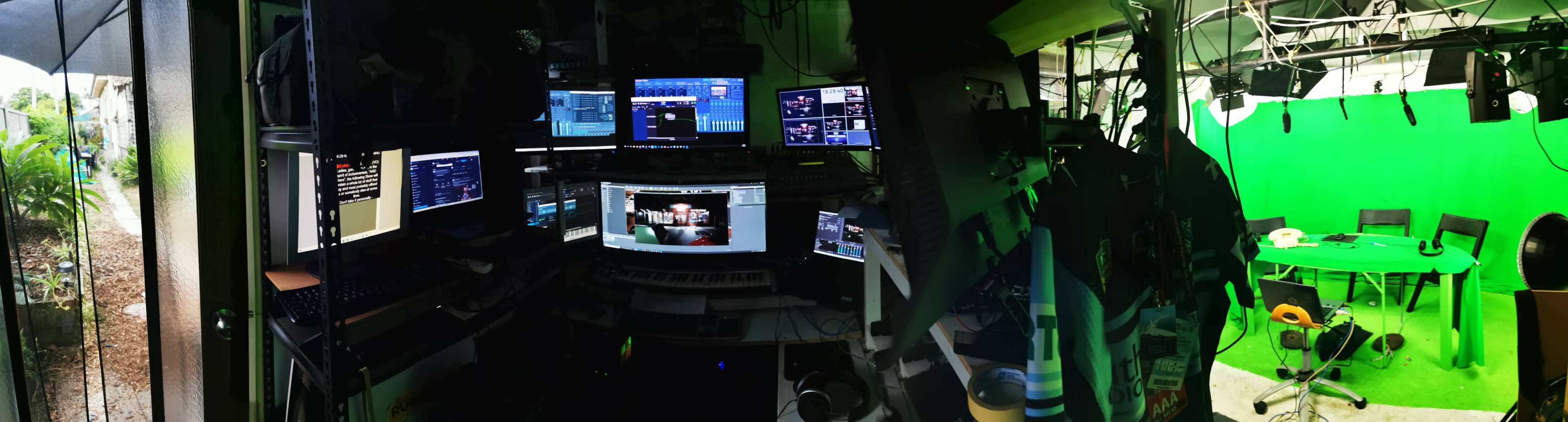 A media production room featuring multiple computer monitors, a green screen backdrop, and various equipment arranged in a workspace.