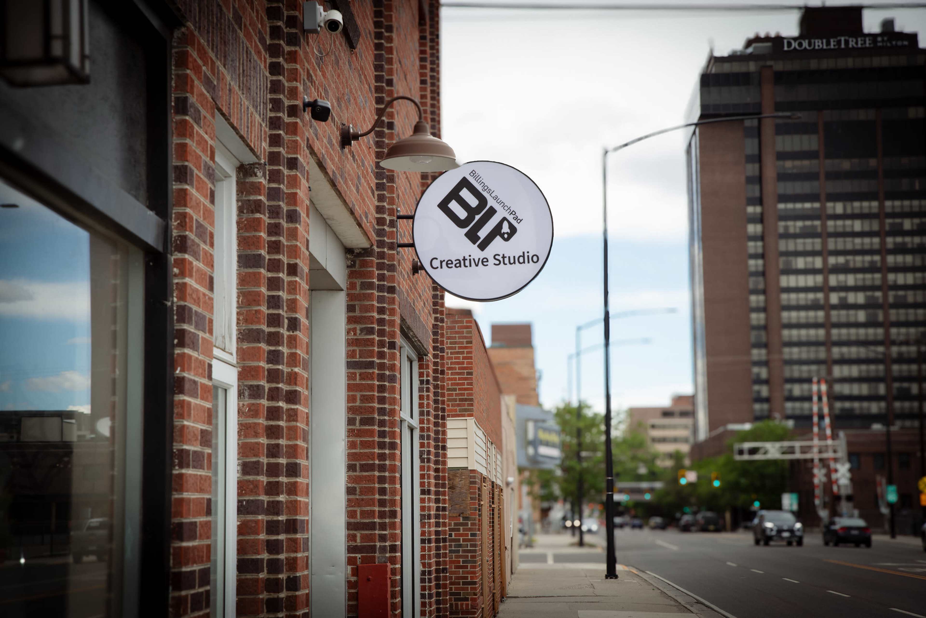 The image shows a round sign for "BIR Creative Studio" hanging from a brick building, with a street and tall buildings visible in the background.