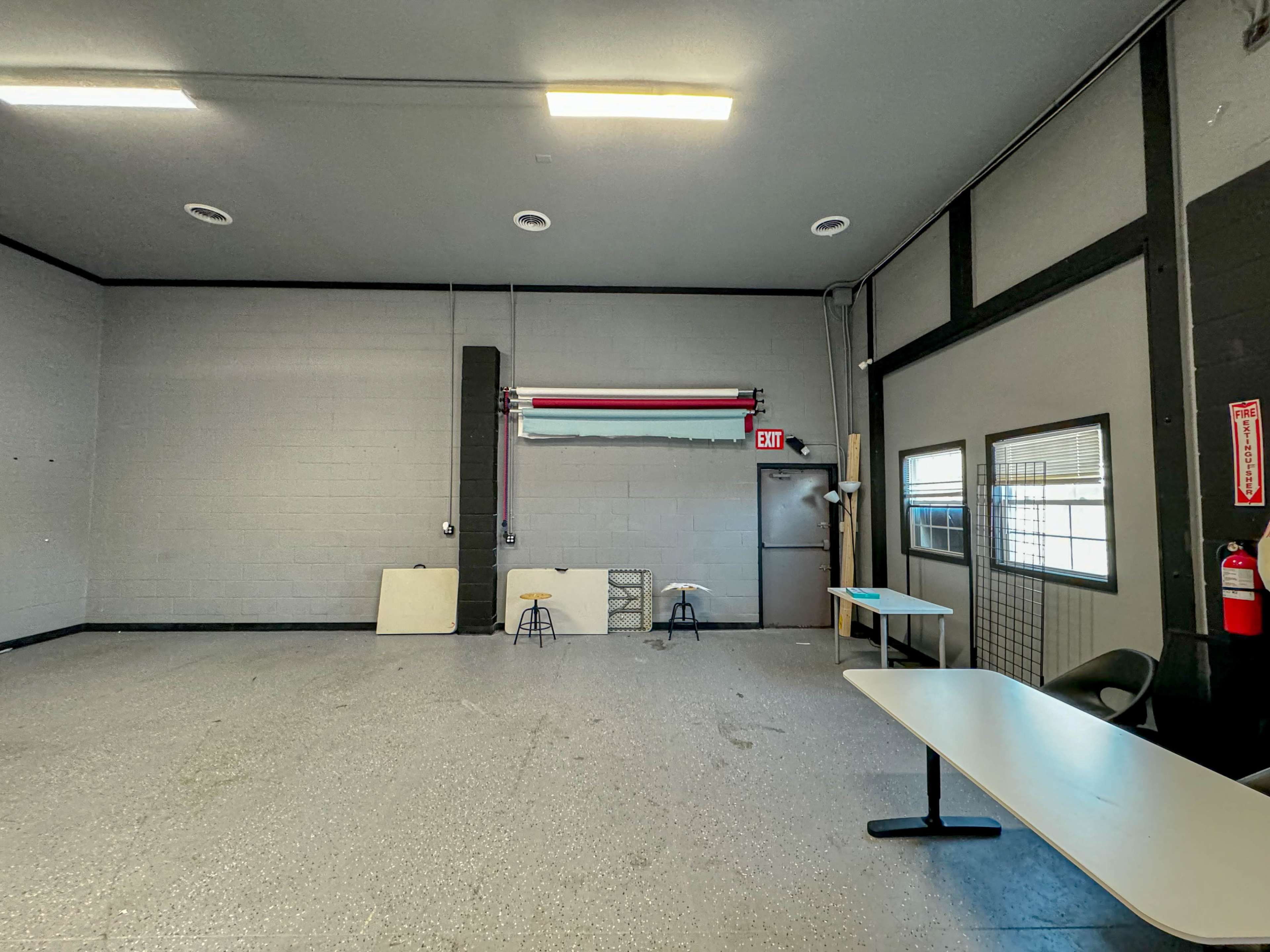 An empty industrial space with a roll-up door, two folding chairs, and a table set against a gray wall.