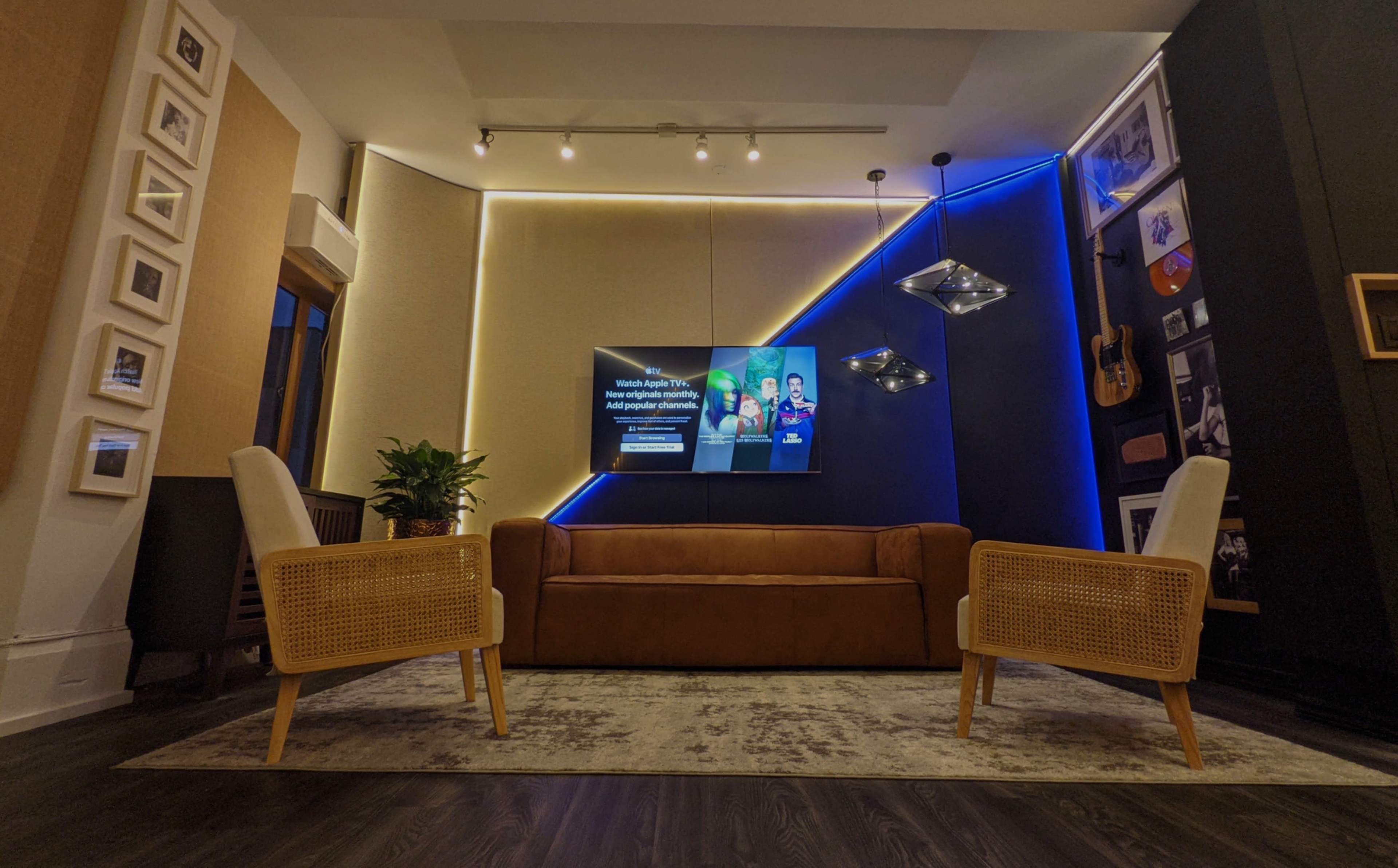 A modern living room features a brown couch, two wicker chairs, a wall-mounted television, and LED lighting accents.
