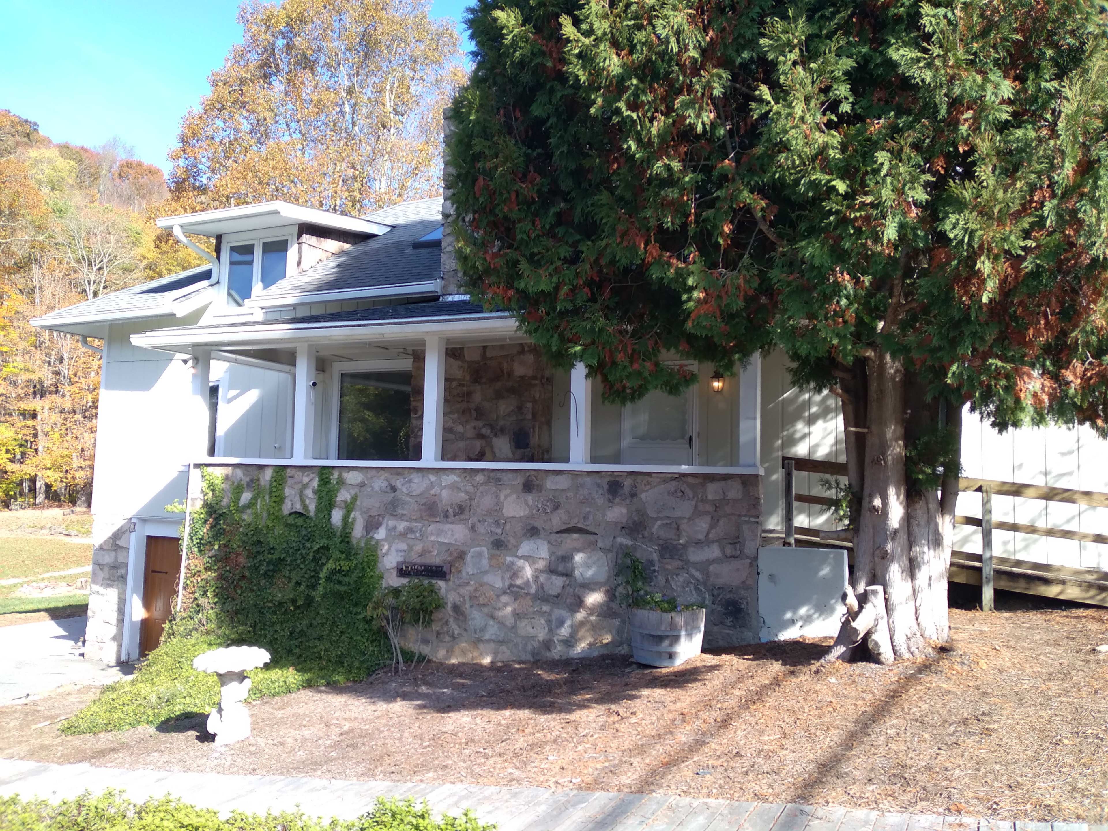 A house with a stone exterior and a large tree in front is surrounded by gravel pathways and landscaping.